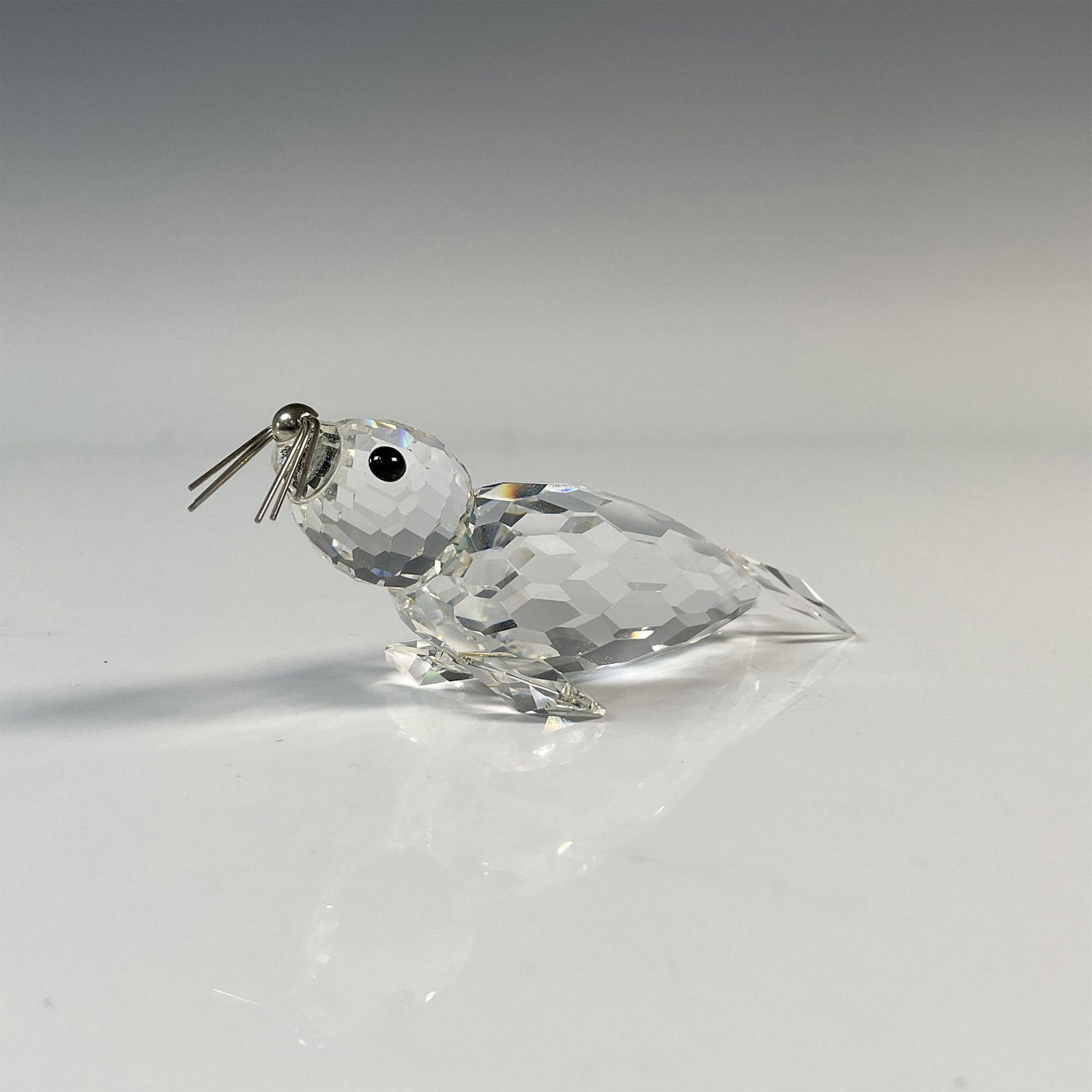 Swarovski Crystal Figurine, Seal with Metal Whiskers: Beautiful facetted clear crystal featuring spread-out flippers, black crystal eyes, and rhodium whiskers. Swarovski backstamp. Includes the original box, dimensions: 6.5"H x 3.25" dia. Artist: Max Sch