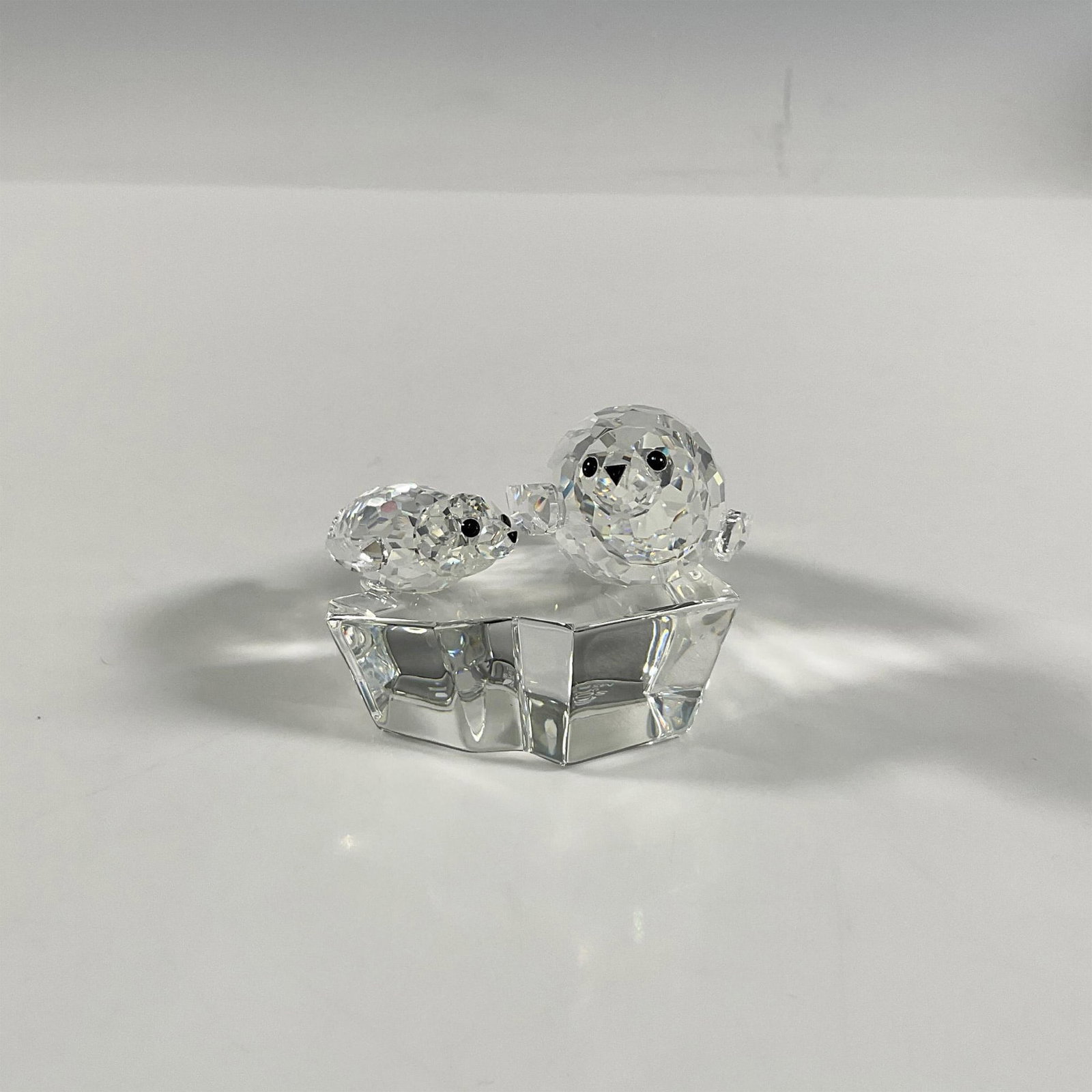 Swarovski Crystal Seals Figurine, Save Me: A clear faceted figure of a mother seal and her pup, both with black eyes and nose, resting atop a clear smooth ice floe. 1991 Swarovski Collectors Society edition. Part of the Mother and Child series
