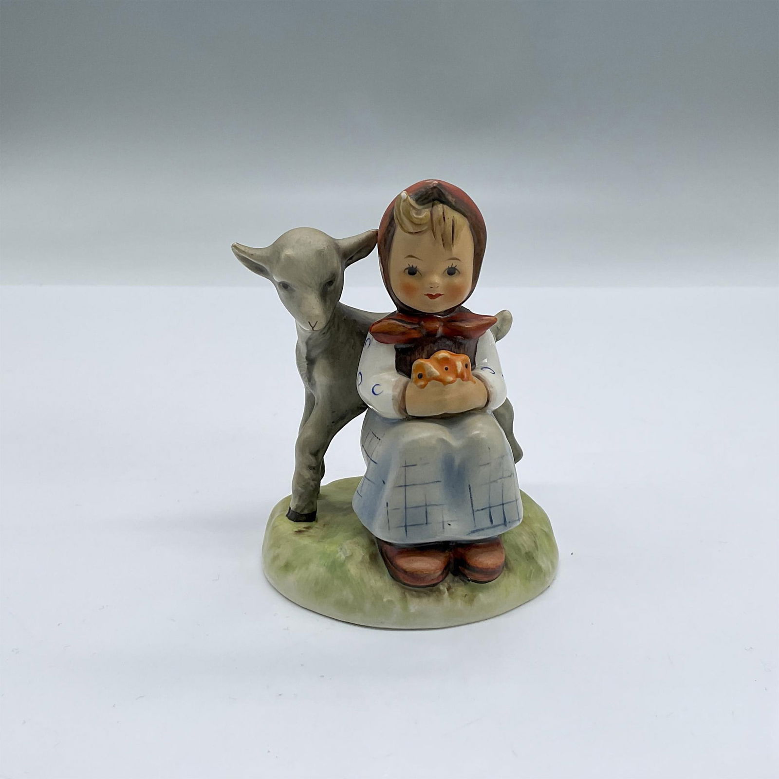 Goebel Hummel Figurine, Good Friends: Beautifully hand painted porcelain figurine of a charming little girl holding a small floral bouquet that matches her red dotted babushka, as a wee grey goat stands beside her, looking over her should