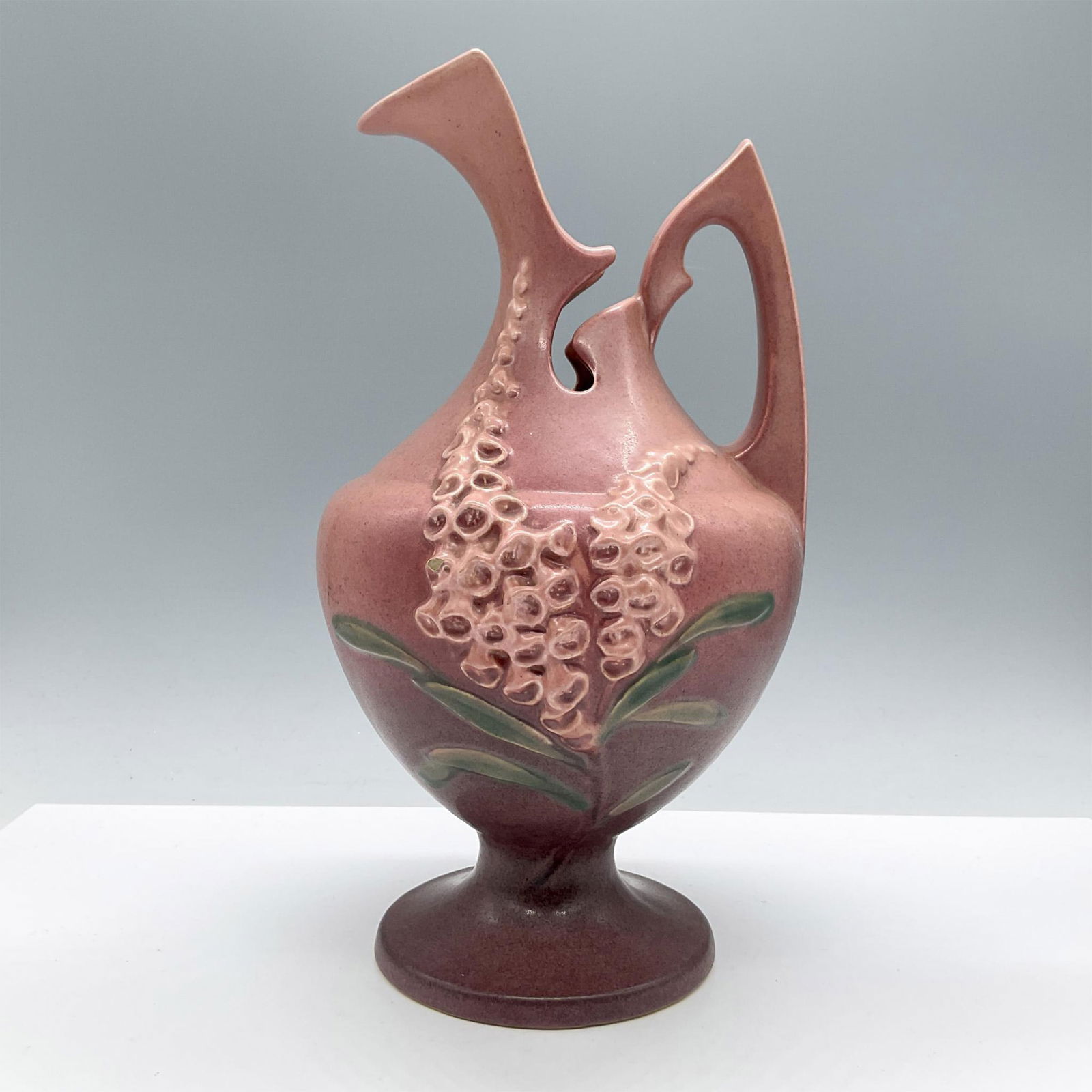 Roseville Pottery Pink Water Pitcher, Foxglove 5-10: Features a relief tapering blossom cluster of pink flowers pattern on a deep pink background. Roseville backstamp. Issued: 20th century Dimensions: 10.75''H x 6''dia Manufacturer: Roseville Country of