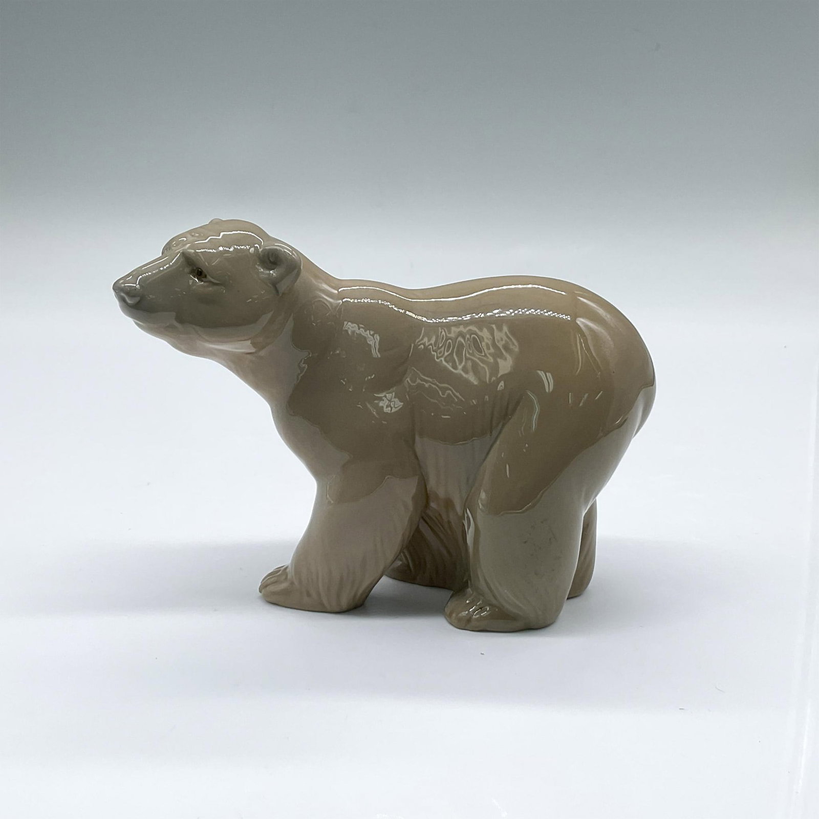 Lladro Porcelain Figurine, Attentive Bear 1001204: Glossy animal figure of a brown bear. Lladro backstamp. Artist: Juan Huerta Issued: 1972-1989 Dimensions: 5"L x 2.5"W x 3.75"H Manufacturer: Lladro Country of Origin: Spain