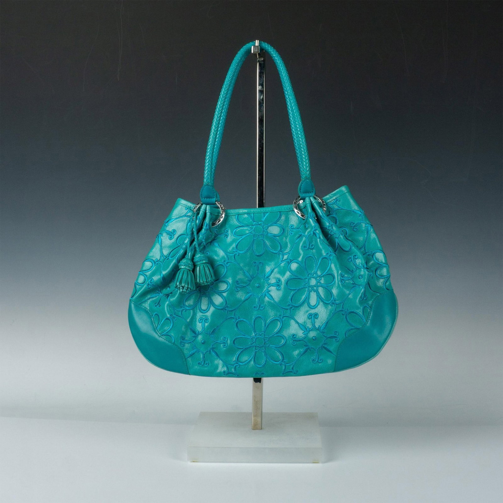 Brighton Teal Leather and Floral Embroidered Handbag: Magnetic closure opens to fabric lining and additional pockets. Leather exterior with floral motif, braided leather shoulder straps, and silver fasteners. Brighton embossed number D9499546. Dust bag i