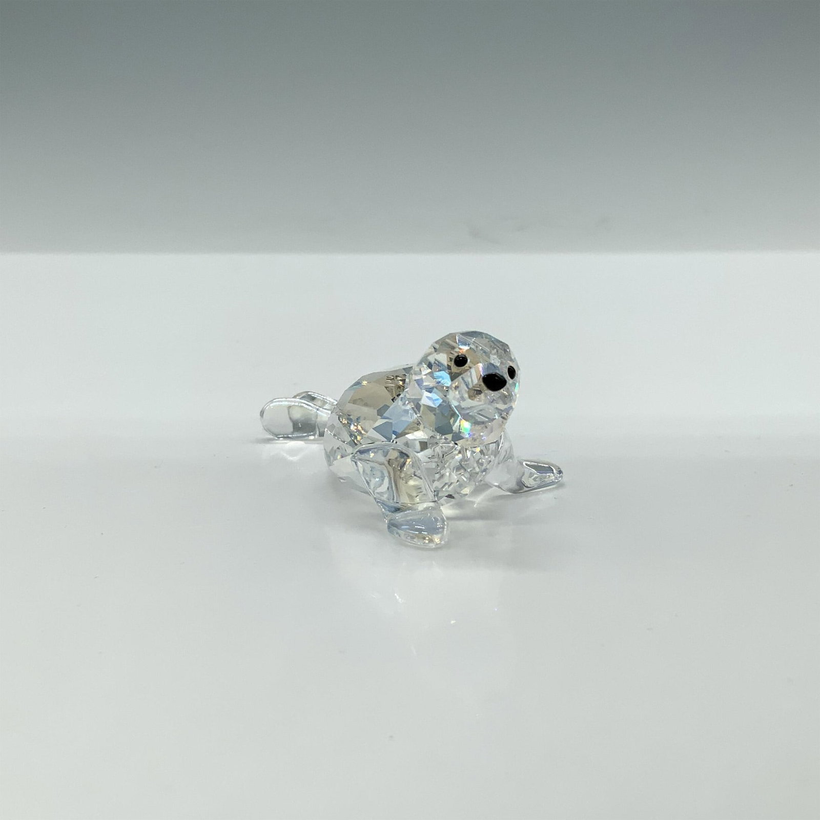 Swarovski Crystal Figurine, 2012 Baby Seal: A clear faceted figure of a seal pup with a shimmering iridescent sheen, featuring black eyes and nose. 2012 SCS Exclusive. Artists signature inscription. Swarovski etched marking. This item has its o