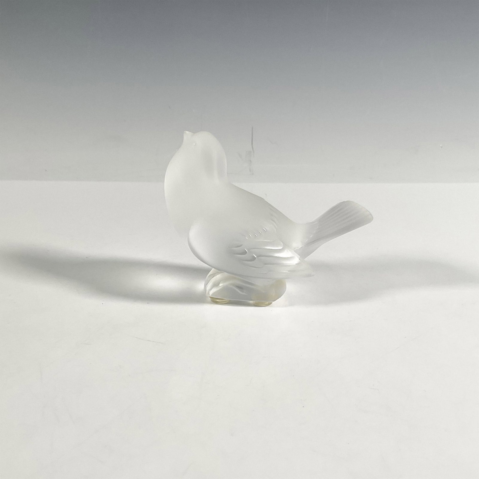 Lalique Crystal Figurine, Sparrow: A delicate frosted sparrow facing upwards in a moment of serene grace. Lalique backstamp. Marked France. Dimensions: 4.25"L x 2.5"W x 3.5"H Manufacturer: Lalique Country of Origin: France
