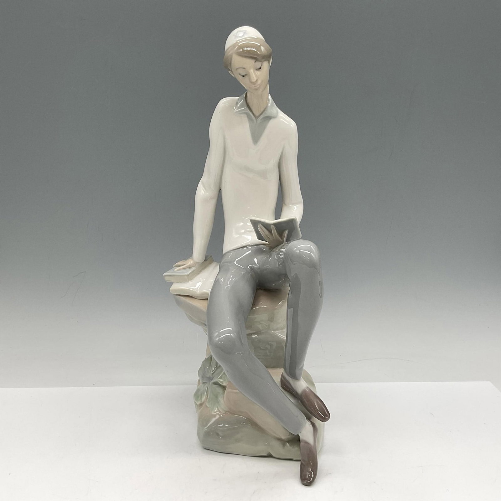 Hebrew Student 1004684 - Lladro Porcelain Figurine: Glossy Judaica figure of a young man seated on a boulder reading. Lladro backstamp. Artist: Juan Huerta Issued: 1970 - 1985 Dimensions: 6"L x 4.5"W x 11.5"H Manufacturer: Lladro Country of Origin: