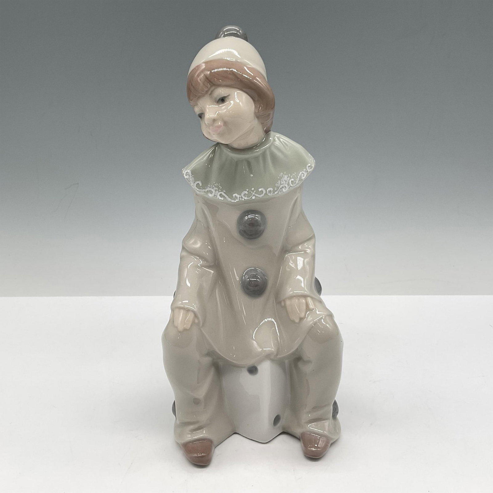 Girl with Dice 1001176 - Lladro Porcelain Figurine: Glossy figural of a girl sitting on a die with her hands resting on her thighs. Lladro backstamp. Artist: Juan Huerta Issued: 1971 - 1981 Dimensions: 3.5"L x 2.5"W x 8"H Manufacturer: Lladro Country