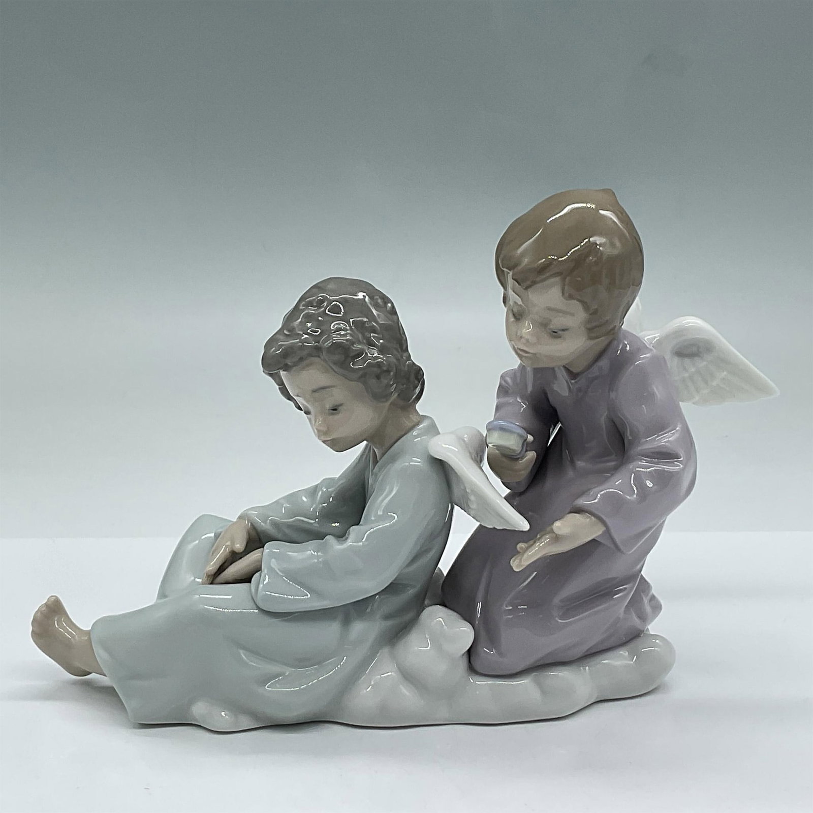 Angel Care 1005727 - Lladro Porcelain Figurine: Glossy finish porcelain depicting two celestial angels resting on a cloud as one brushes the other's wings. Lladro backstamp. Artist: Fulgencio Garcia Issued: 20th c. Dimensions: 7.25"L x 2.5"W x 5"H 
