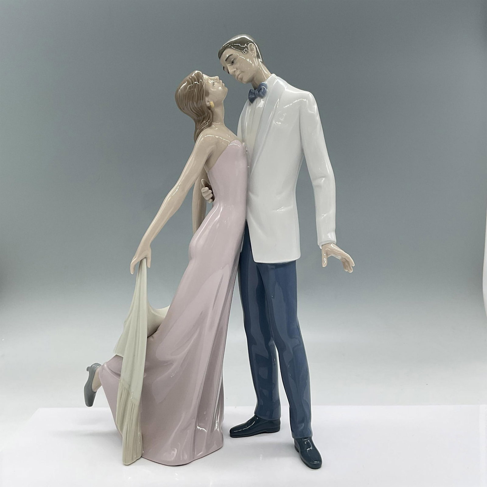Happy Anniversary 1006475 - Lladro Porcelain Figurine: Glossy, hand made porcelain, modeled in elegant pale pastel colors. Depicts a romantic scene of two lovers looking into each other's eyes. The woman is dressed in a flowing soft pink dress holding beh