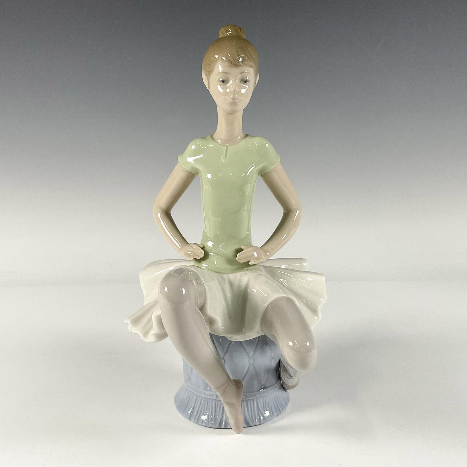 Laura 1001360 - Lladro Porcelain Figurine: A glossy figure of seated woman a wearing a sage green top and white tutu. Lladro backstamp. Artist: Juan Huerta Issued: 1978-1993 Dimensions: 4.5"L x 6"W x 9"H Manufacturer: Lladro Country of Origin