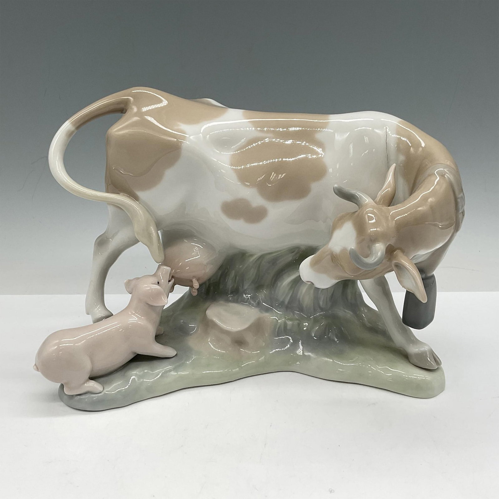 Cow with Pig 1004640 - Lladro Porcelain Figurine: Glossy figurines in pasture, colored in pale brown, white, sage and pink. Lladro backstamp. Artist: Vincente Martinez Issued: 1969 - 1981 Dimensions: 8"L x 4.5"W x 6"H Manufacturer: Lladro Country of