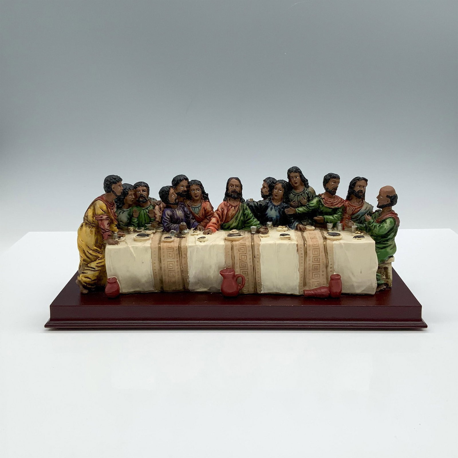 Vintage The Last Supper Figurine: A figure with a wooden base portraying Jesus and his disciples gathered around a long table filled with food and drinks. Dimensions: 10.25"L x 4"W x 4"H