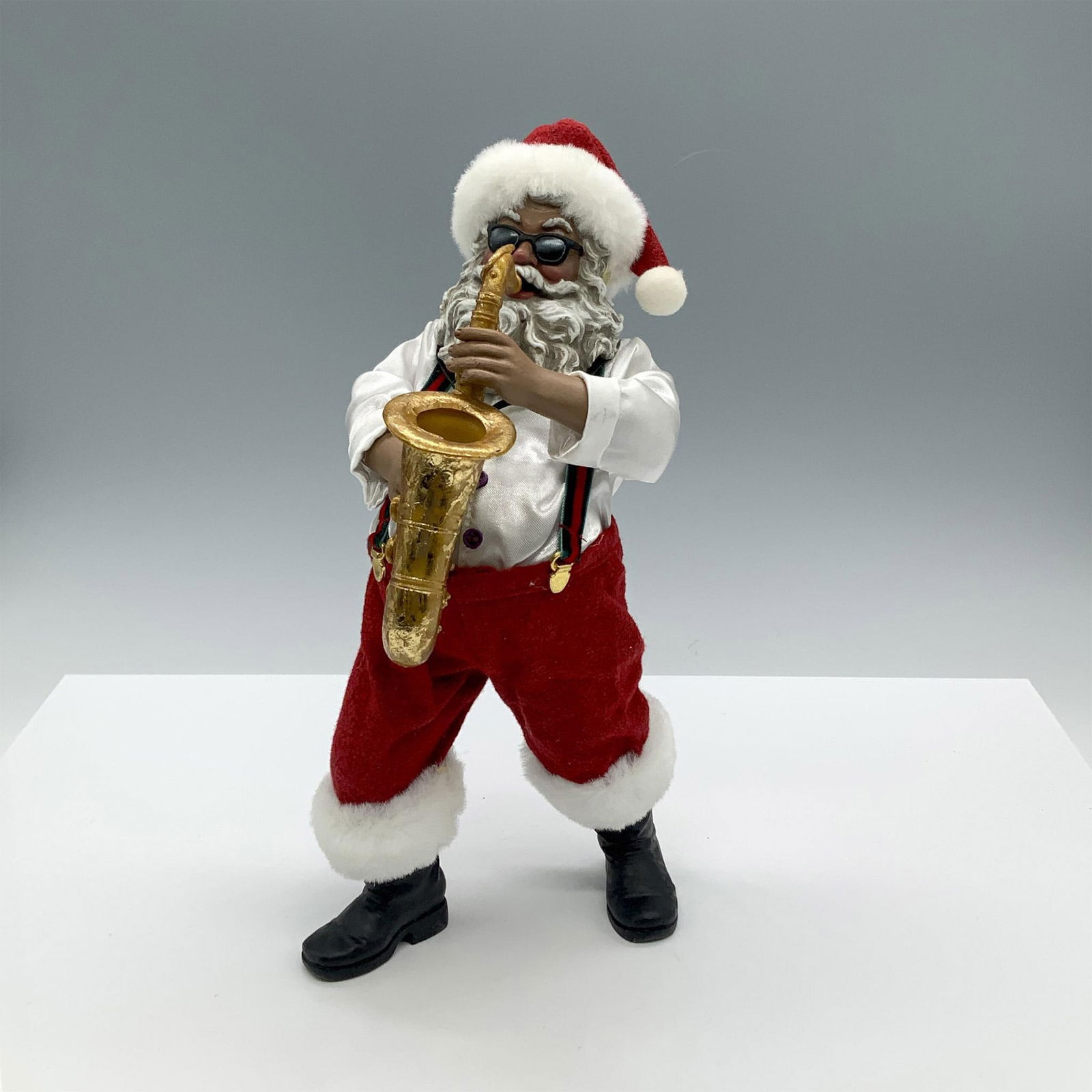 Department 56 Possible Dreams Santa Playing Saxophone: A whimsical Holiday figurine featuring Santa Claus wearing sunglasses and putting on a performance as he plays the saxophone with flair. PD impressed marking. Artist: Ann Dezendorf Dimensions: 5.5"L x