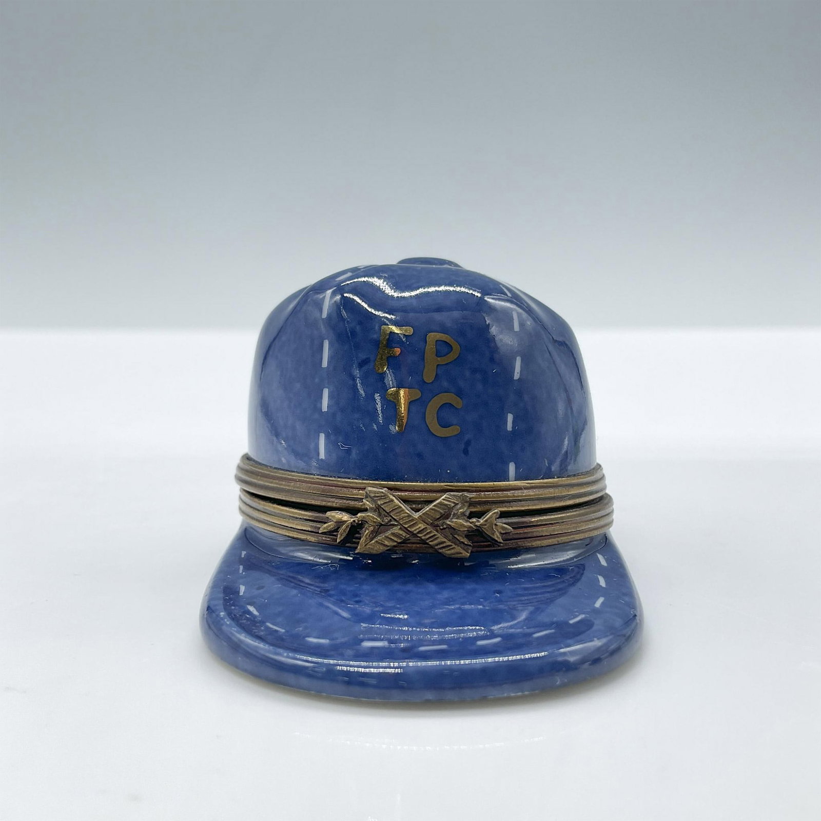 Limoges Porcelain Treasure Box, Baseball Hat: Hand painted in Limoges France. Features a blue hat with white stiches, completed by a metal closure. Signed Peint Main Limoges France GR. Issued: 20th century Dimensions: 2.5''L x 1.75''W x 1.5''H Co