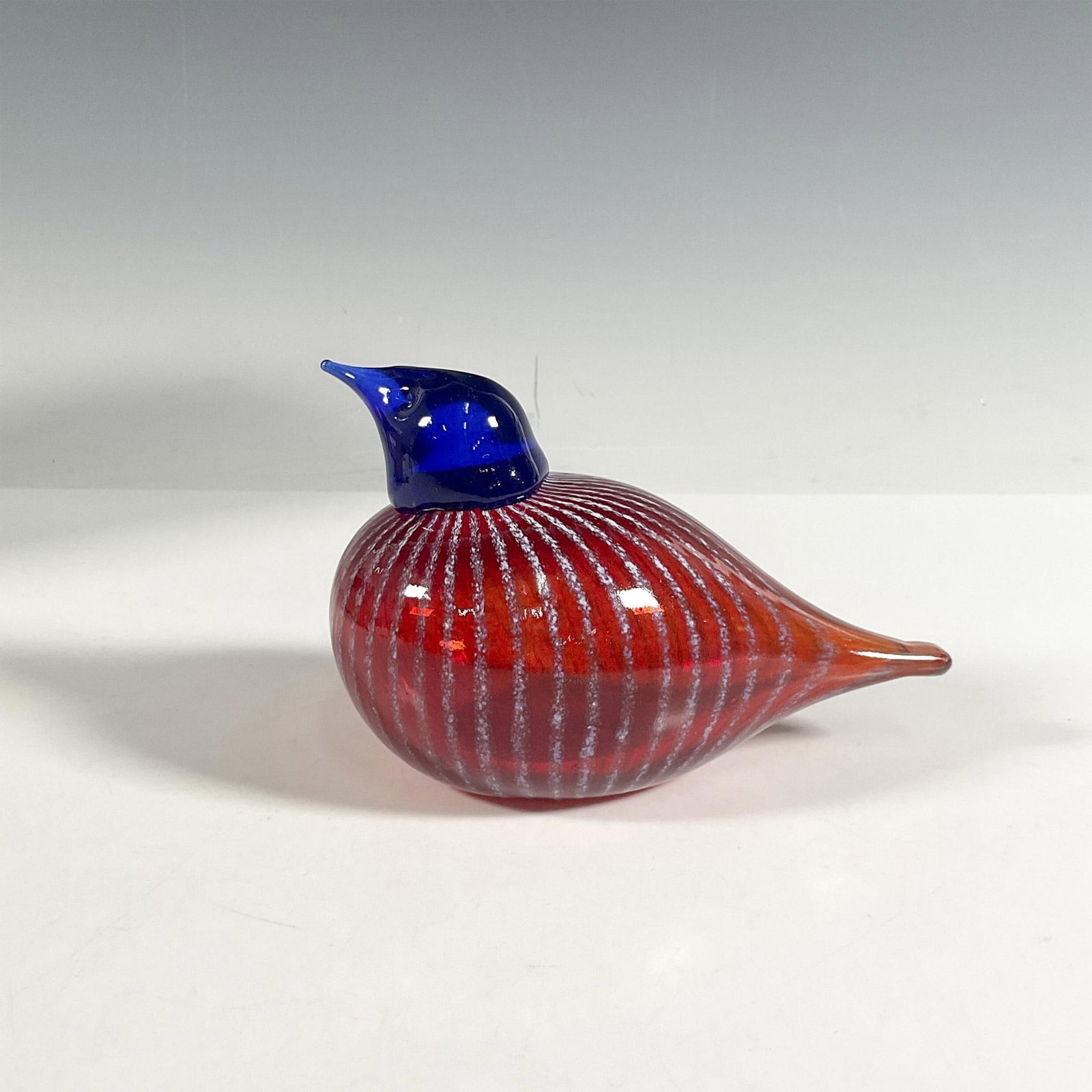 Bianco Blue Glass Figurine, American Red Willow: A handcrafted glass bird featuring a round body in vibrant red with delicate white stripes, topped by a striking blue head. Artist signature. Bianco Blu manufacturing sticker. This item has its origin