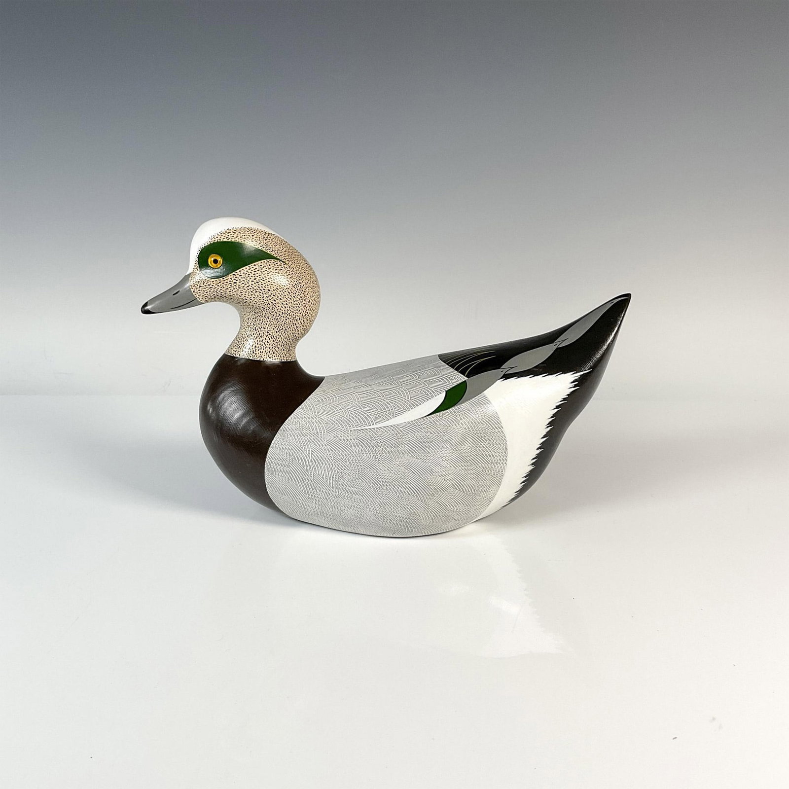 Dave Frier Wooden Duck Decoy, Wigeon: Represents a Wigeon duck characterized by its white crown. Painted with a mix of cream and brown speckling on the head highlighted by a striking green eye patch that extends from the eye towards the b
