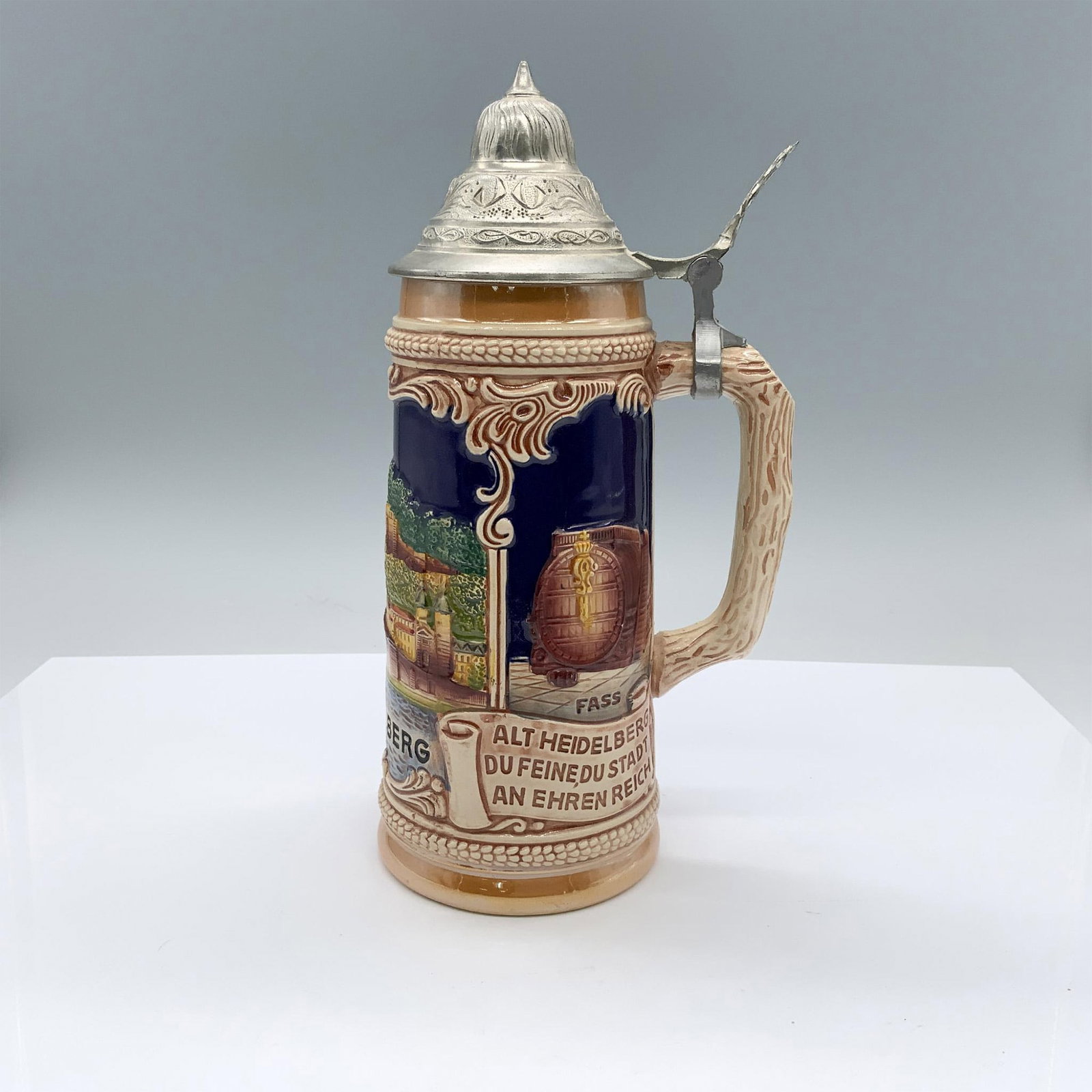 Vintage Handgemalt Heidelberg Beer Stein: A ceramic drinking vessel with a raised design depicting scenery from the city of Heidelburg, scrolls with German phrases, and a handle with the texture of wood. Handhemalt backstamp. Weight: 1.15 lb.
