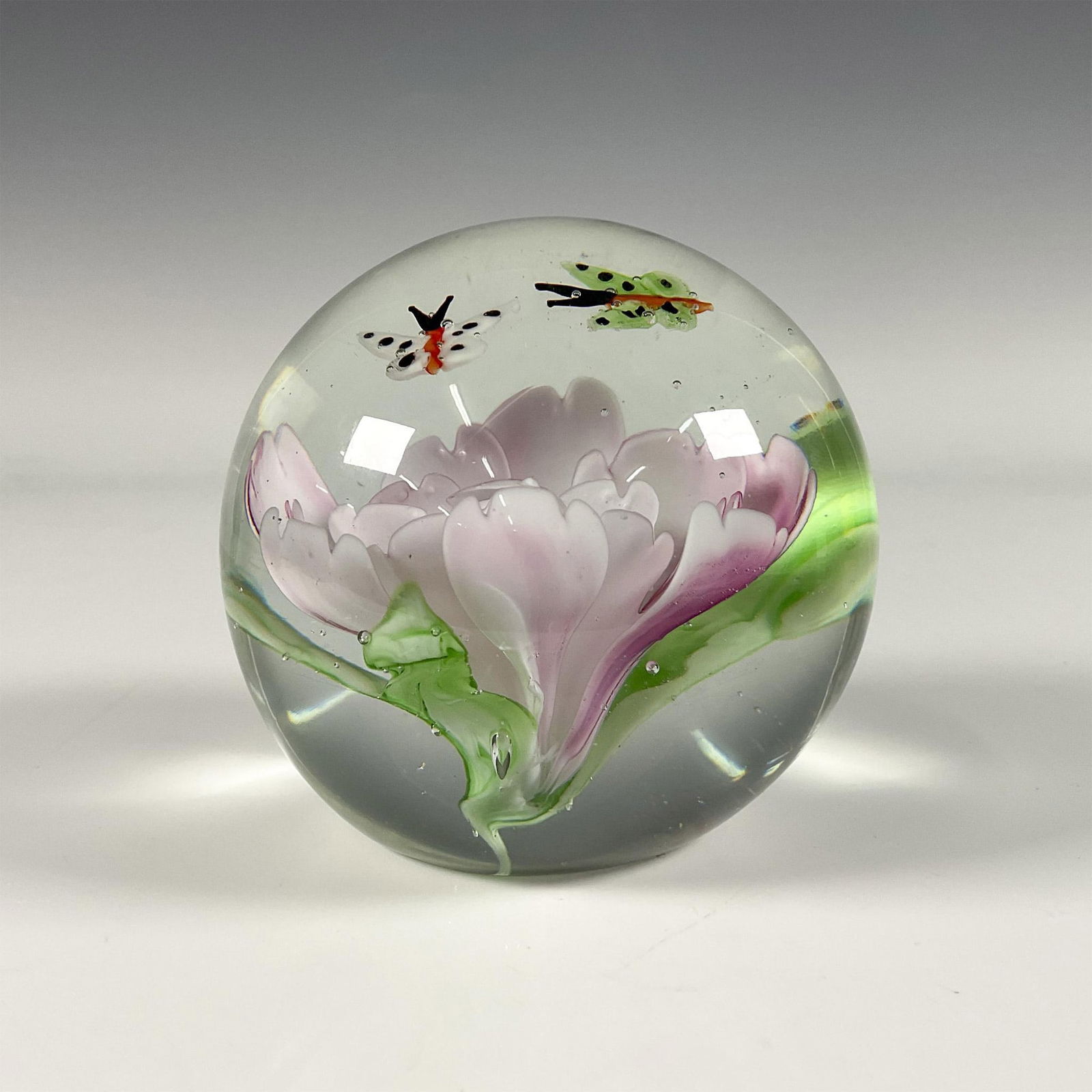Art Glass Paperweight: Beautiful floral and butterfly design in clear glass. Flower is pink with green leaves and butterflies are white and green with spots. Issued: 20th century Dimensions: 3.5"H x 3.5"dia.