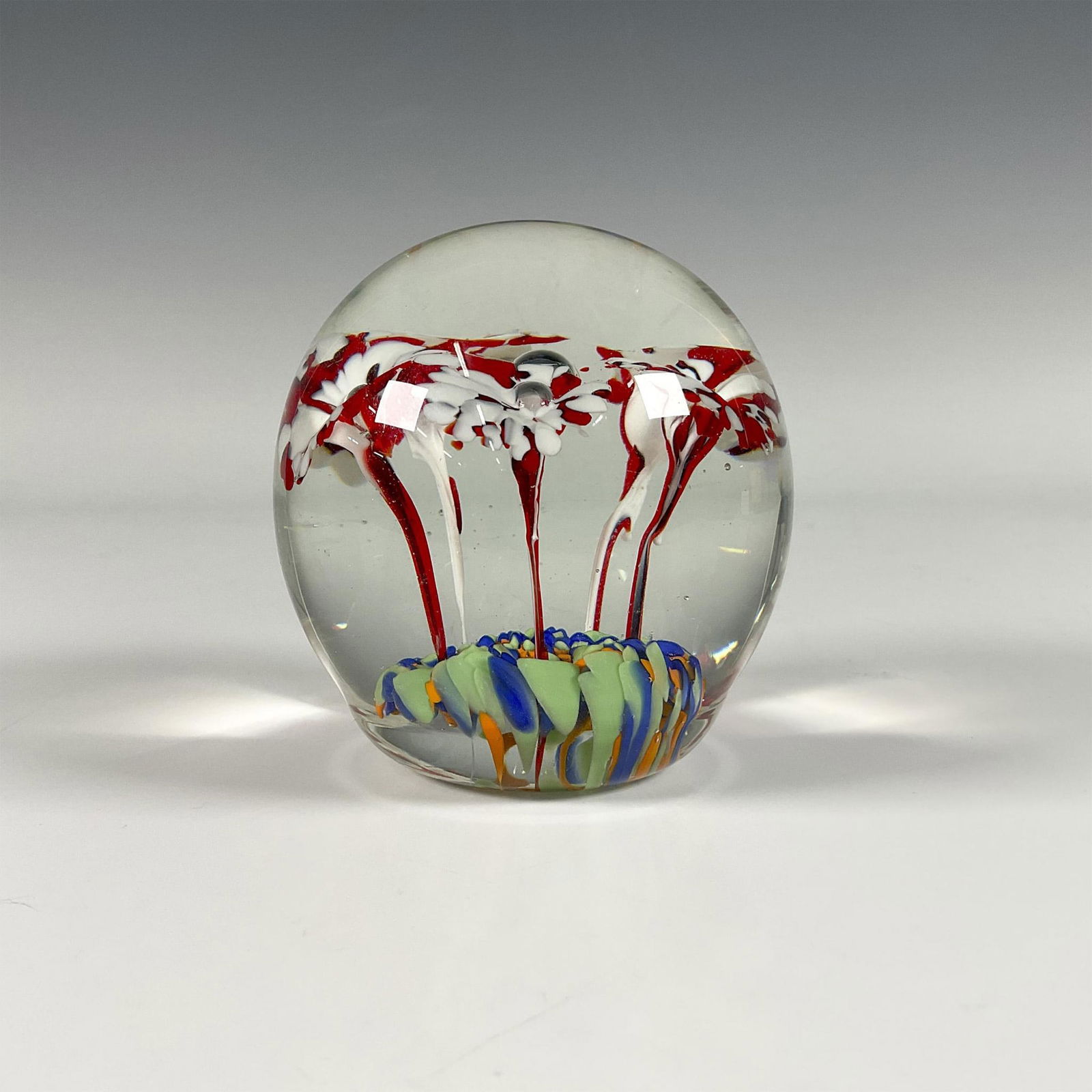 Art Glass Paperweight: Clear globe has delicate red and white flowers growing out of a blue, green, and orange base. A single bubble rises in the middle of the flowers. Issued: 20th Century Dimensions: 3.5"H x 3.25"dia.
