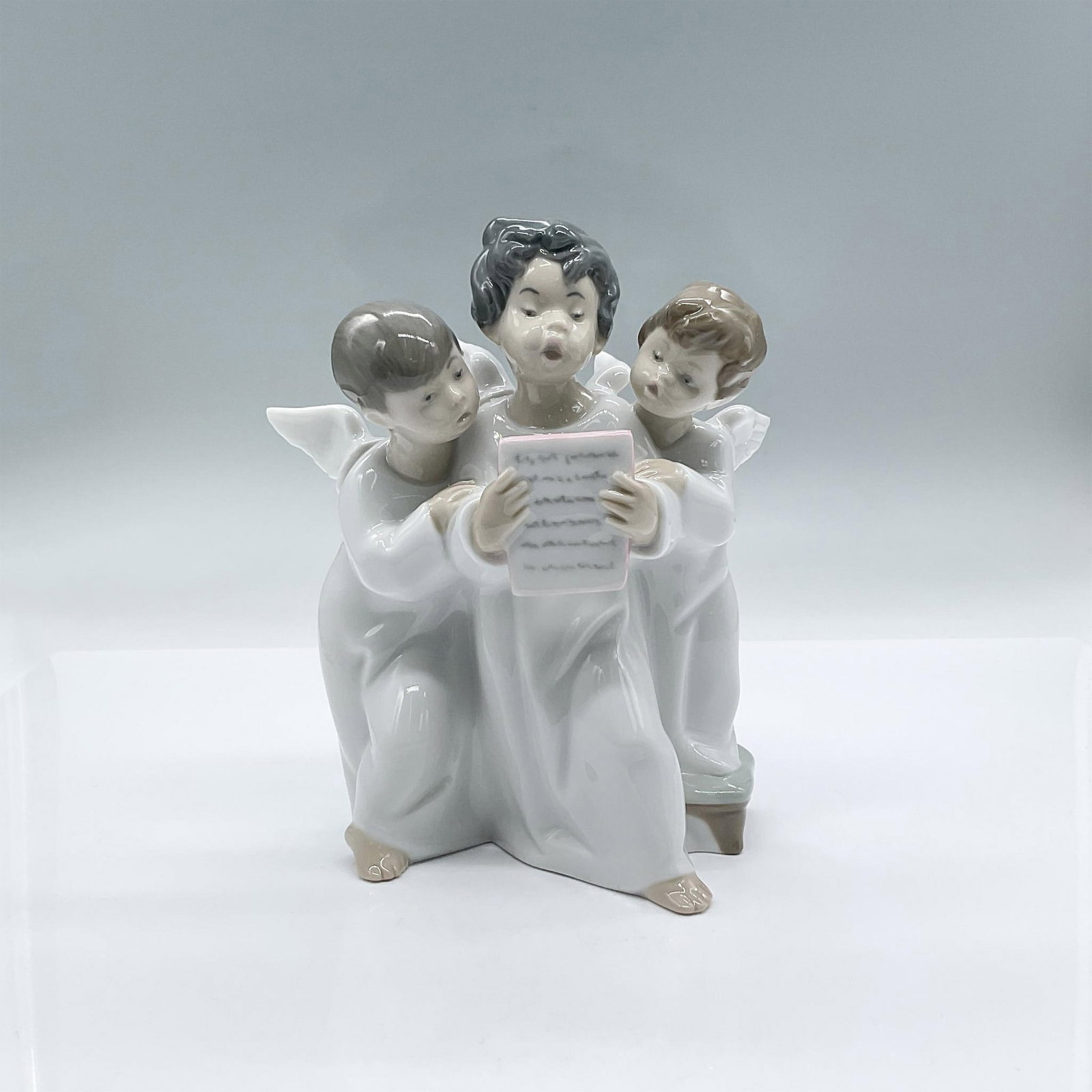 Angels Group 4542 - Lladro Porcelain Figurine: A glossy figure of a trio of young angels wearing long white dresses singing as they look at a music sheet. Lladro backstamp. This item has its original box: 9"L x 6"W x 10"H. Artist: Fulgencio Garcia