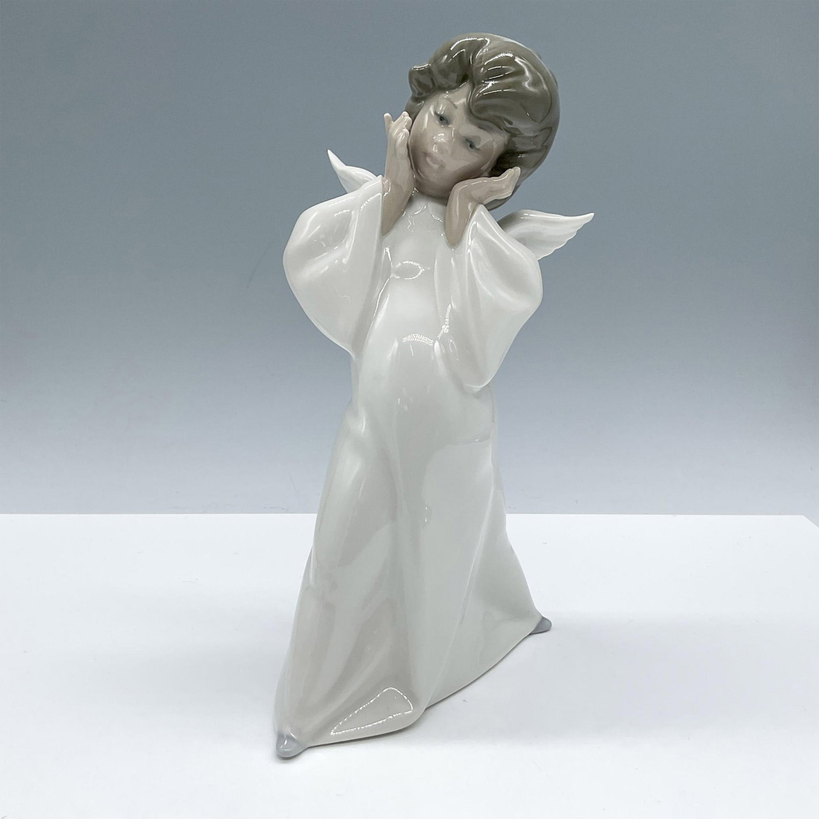 Cherub, Puzzled 1004959 - Lladro Porcelain Figurine: Glossy porcelain. Features a lovely angel dressed in a white gown and wings. Lladro backstamp. Artist: Salvador Debon Issued: 1977 Dimensions: 5''L x 4.5''W x 8.75''H Manufacturer: Lladro Country of