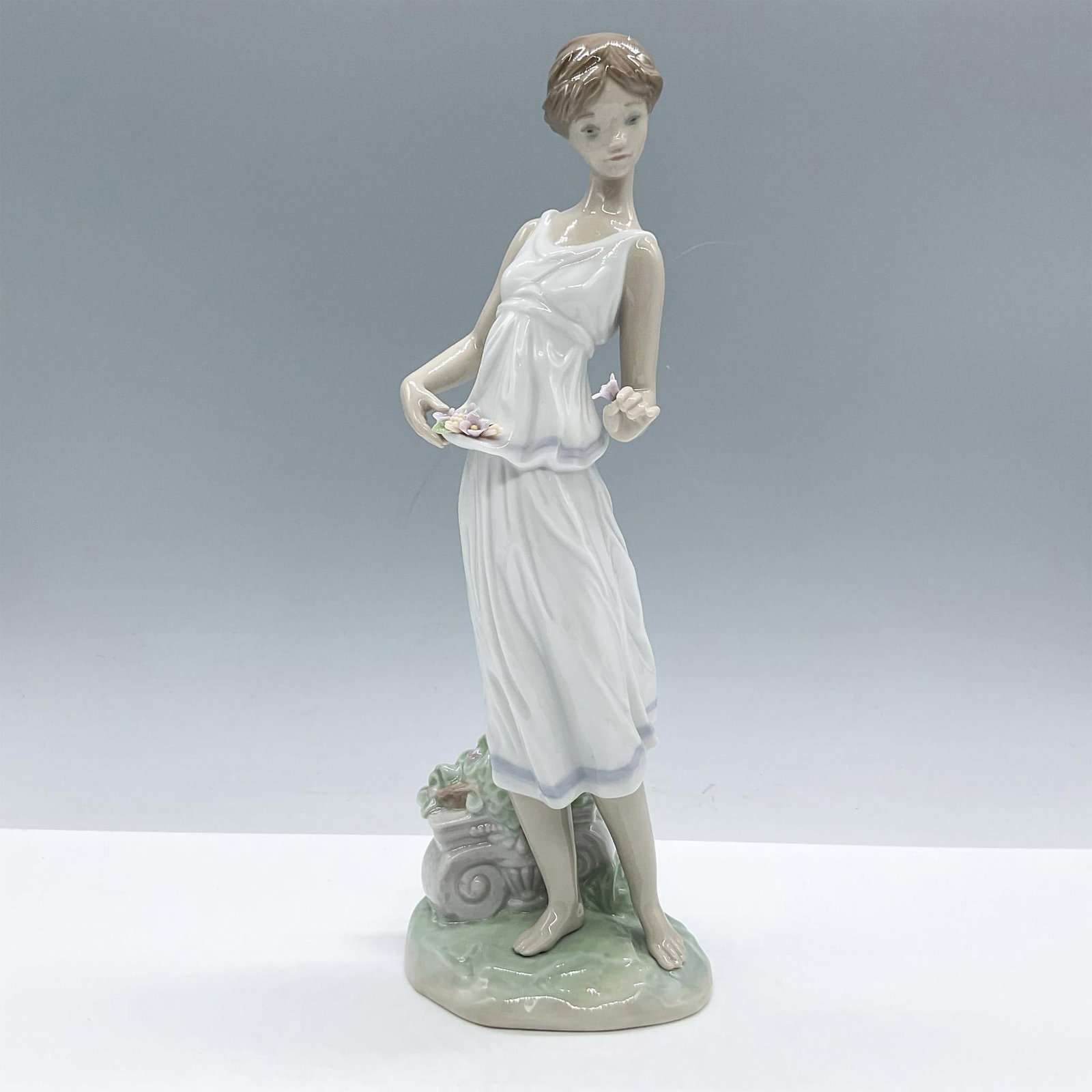 Flowers for a Goddess 1007709 - Lladro Porcelain Figurine: Glazed finish. Depicts a lady in a white Greek gown picking detailed flowers. Lladro backstamp. Includes the original box, dimensions: 6.75''L x 13''W x 6.5''H. Artist: Virginia Gonzalez Issued: 2006 