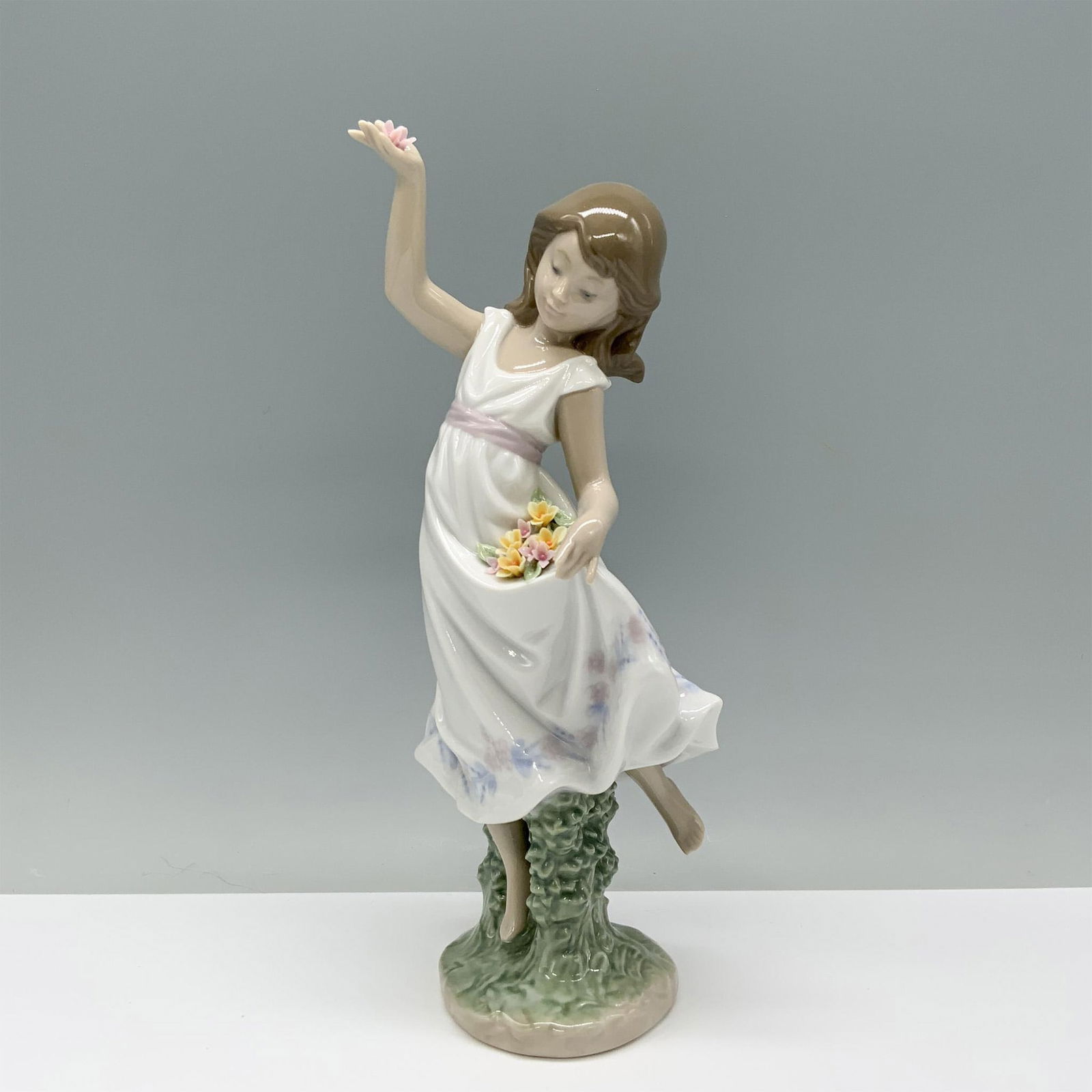 Garden Dance 01006580 - Lladro Porcelain Figurine: A girl in a white sundress holds a bouquet of flowers, using her dress as a makeshift basket. Lladro backstamp. This item has its original box which measures: 11.75"L x 6.5"W x 5.5"H. Artist: Jose Jav