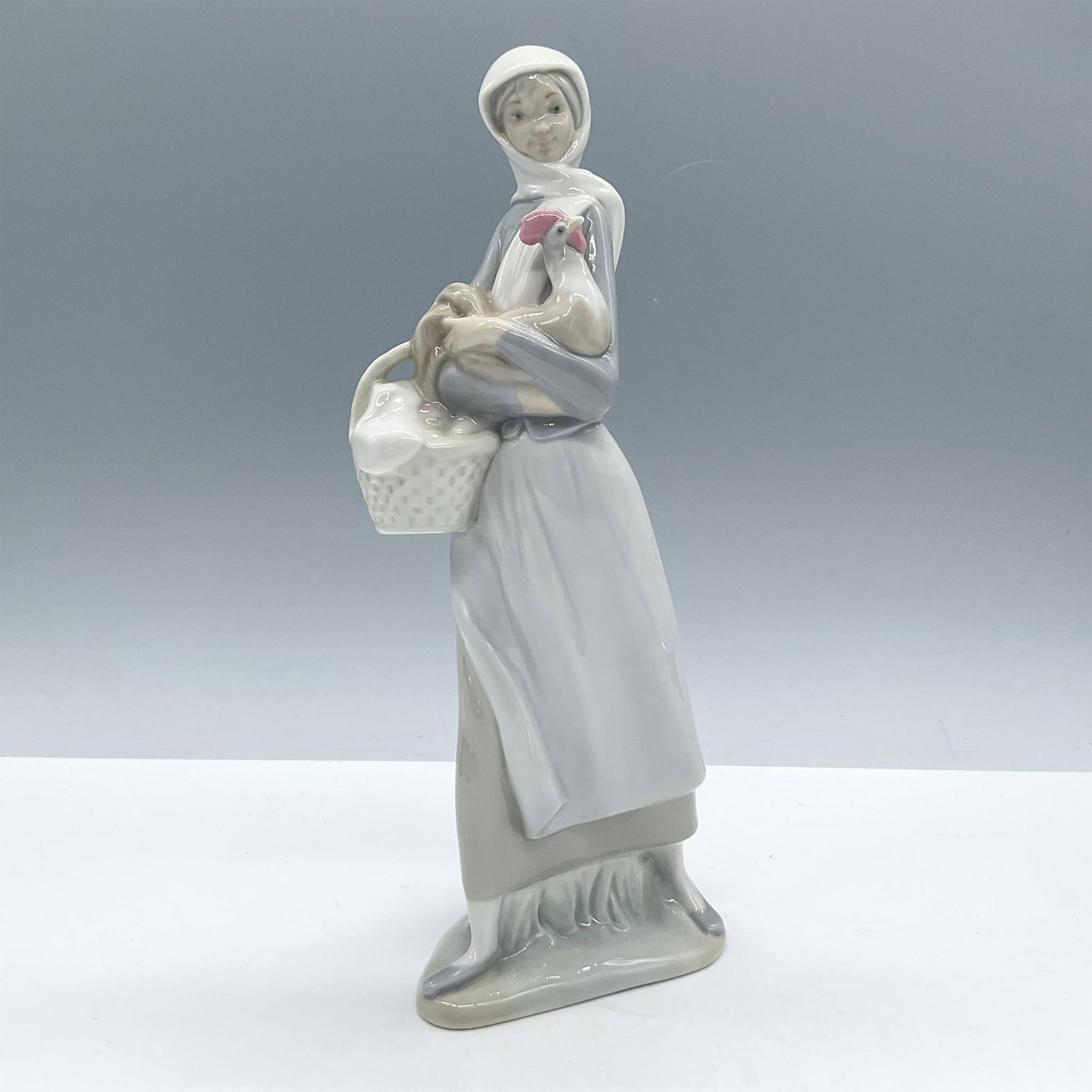 Girl with Cockerel 1004591 - Lladro Porcelain Figurine: Glossy porcelain. Features a country girl holding a cockerel and a basket full of eggs. Lladro backstamp Artist: Fulgencio Garcia Issued: 1969 - 1993 Dimensions: 3.75''L x 2.5''W x 9.5''H Manufacturer