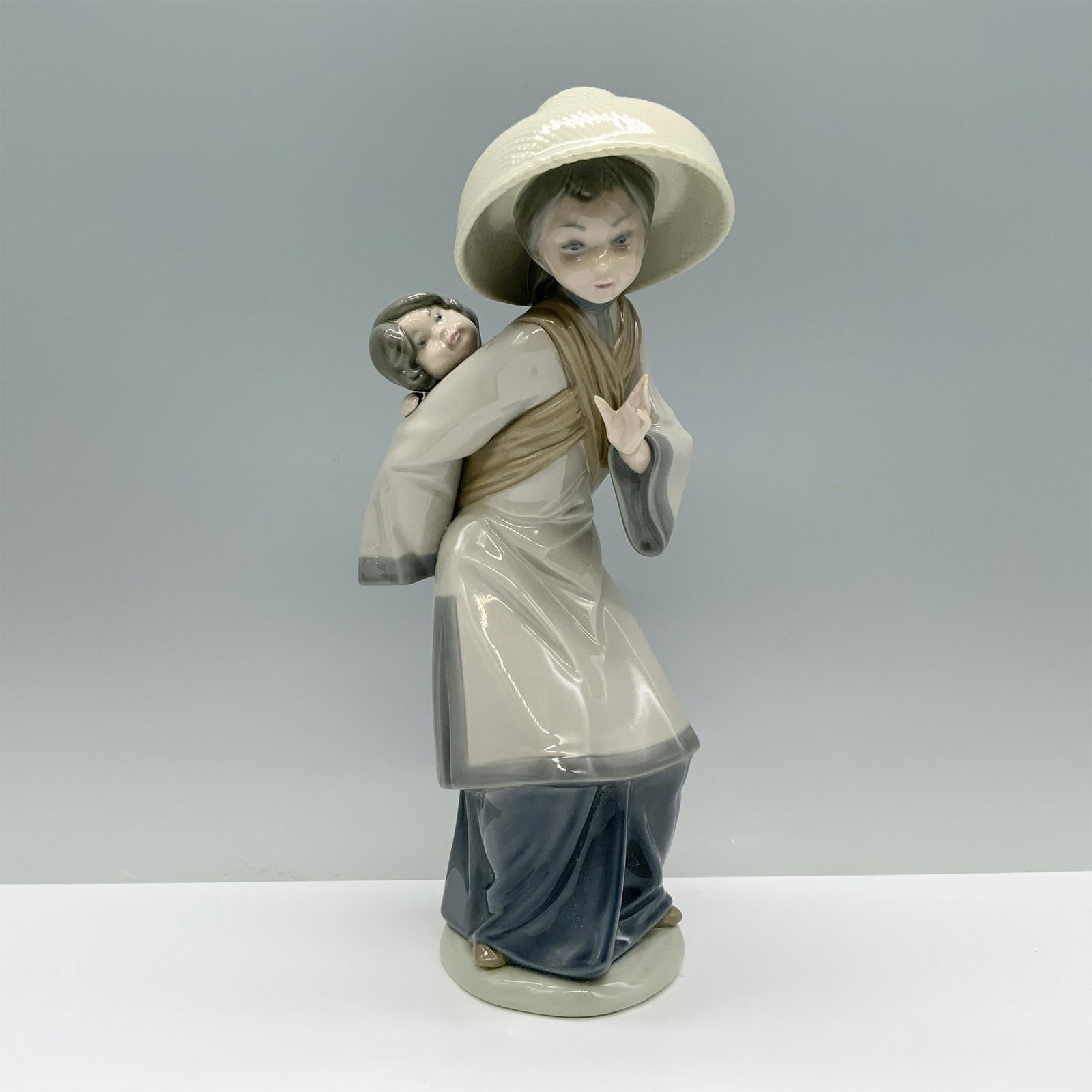 My Precious Bundle 01005123 - Lladro Porcelain Figurine: A mother in a gray robe carries her infant on her back with tender caution. Lladro backstamp This item has a box which measures: 12.75"L x 7.5"W x 6"H. Artist: Salvador Debon Issued: 1982-1998 Dimensi