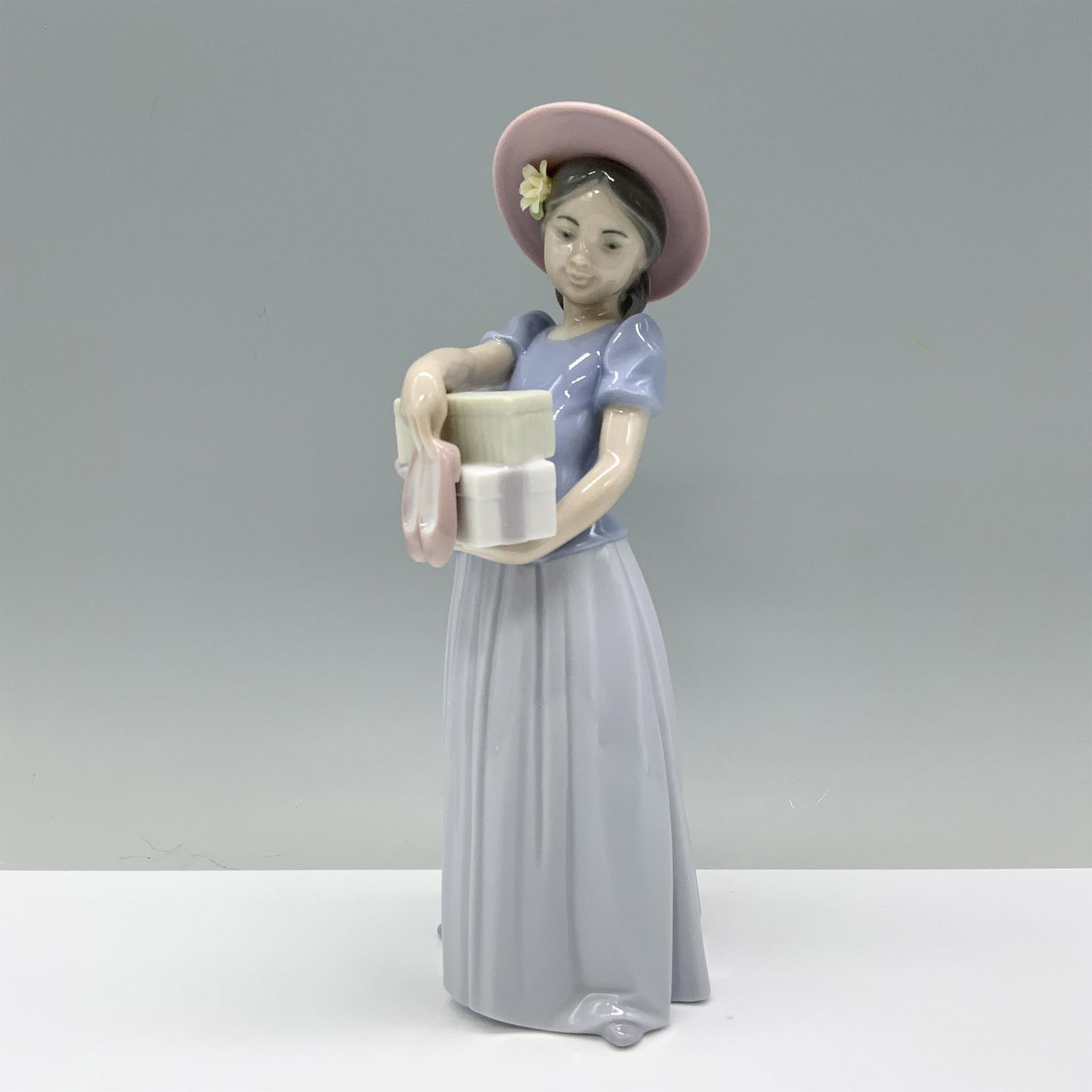 New Shoes 01006487 - Lladro Porcelain Figurine: A young girl in her Sunday best holds a pair of new shoes with excitement. Lladro backstamp. This item has its original box which measures: 11"L x 5.75"W x 5"H. Artist: Marco Antonio Nogueron Issued: 