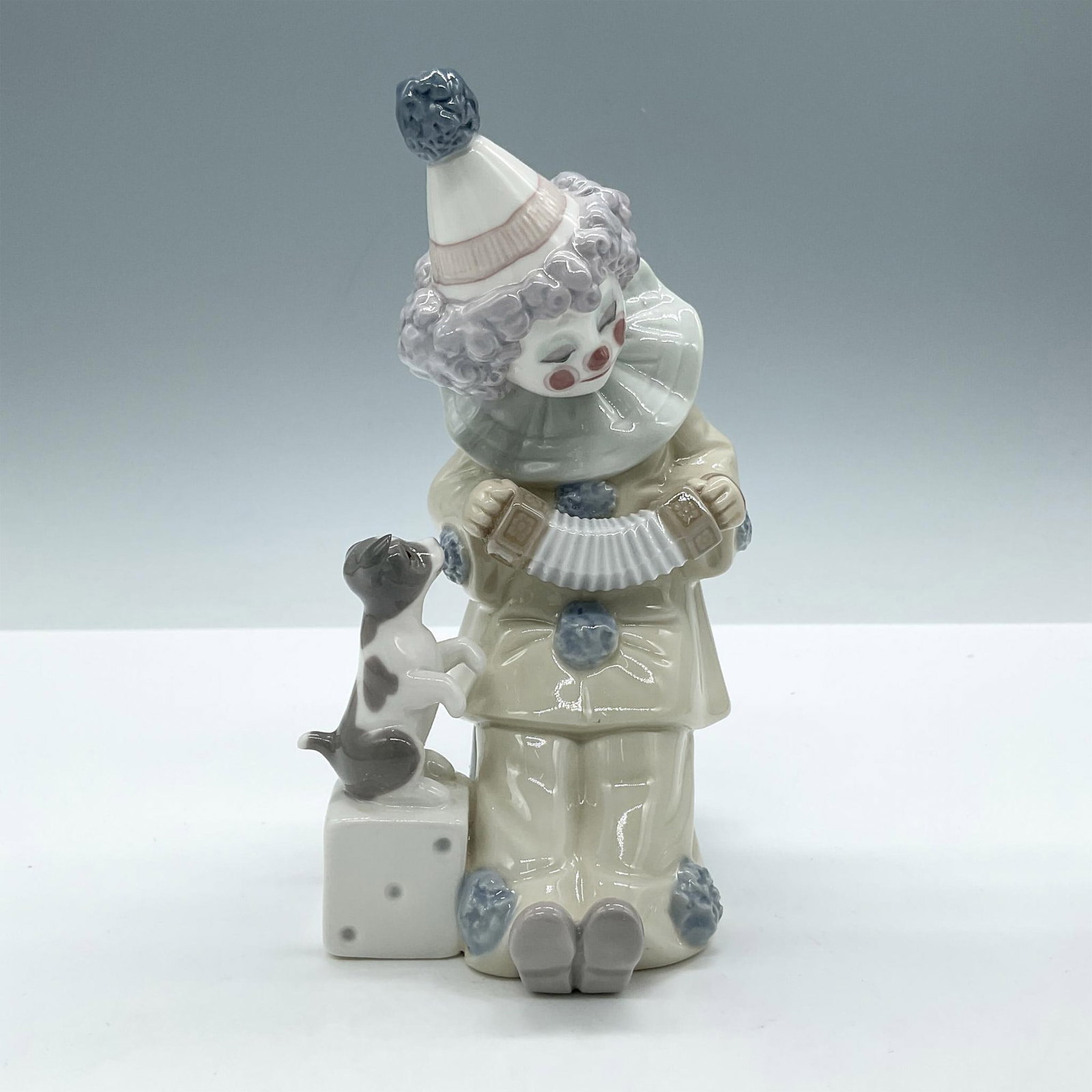 Pierrot with Concertina 1005279 - Lladro Porcelain Figurine: Glossy figural playing his instrument for his dog. Lladro backstamp. This item has its original box: 8"L x 5.5"W x 5"H. Artist: Jose Puche Issued: 1985 - 2007 Dimensions: 3"L x 3.5"W x 6"H Manufacture