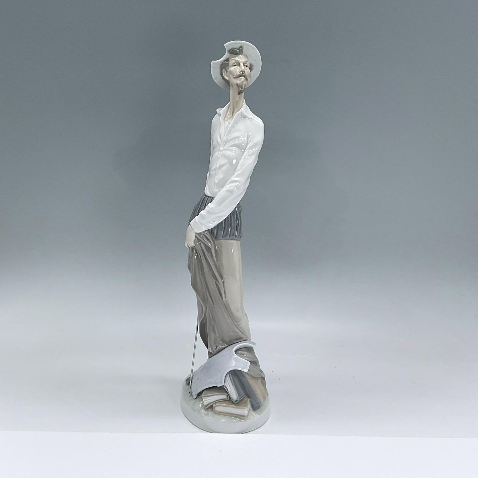 Quixote Standing Up 1004854 - Lladro Porcelain Figurine: Glossy porcelain figure of Don Quixote standing in a white shirt, tan pants and his iconic hat holding a sword in one hand. Lladro backstamp. Includes original box: 17"L x 6.75"W x 6.75"H. Dimensions: