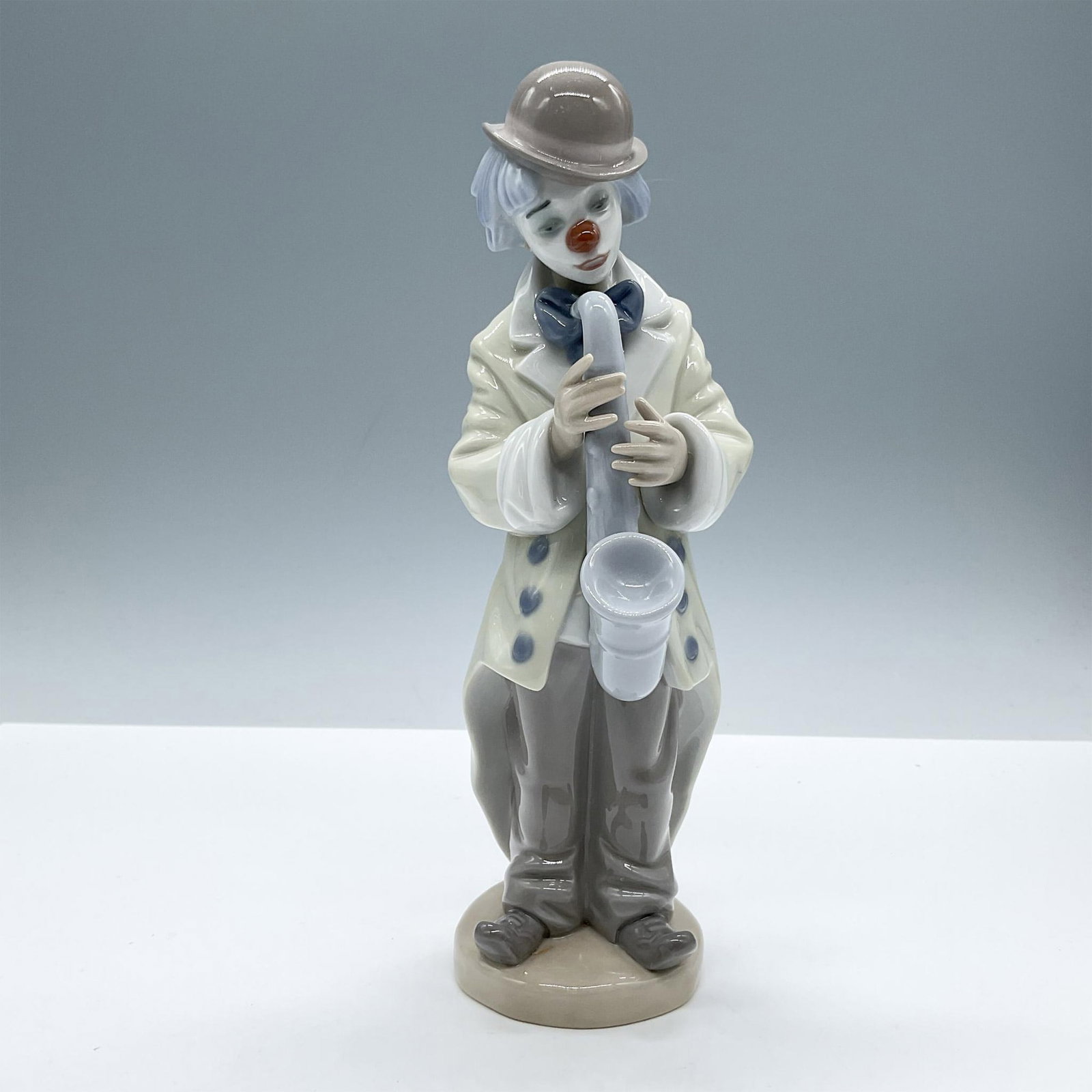 Sad Sax 1005471 - Lladro Porcelain Figurine: A glossy figure depicting a clown in an oversized jacket with a gloomy expression, holding a saxophone. Lladro backstamp. Includes the original box, dimensions: 5.75''L x 10''W x 5.25''H. Artist: Fran