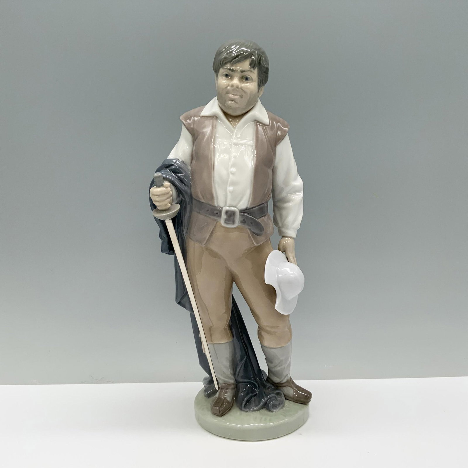 Sancho 01006633 - Lladro Porcelain Figurine: Sancho Panza from Don Quixote, clad in a tan and white outfit, confidently holding his sword. Lladro backstamp. This item has its original box which measures: 11.75"L x 6.5"W x 5.25"H. Artist: Salvado