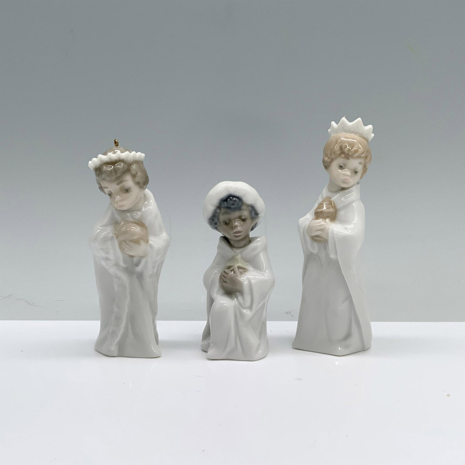 3pc Lladro Porcelain Tree Ornaments, Three Kings 01005729: The three wise men, clad in pristine white robes, hold their gifts in preparation for Baby Jesus. Lladro backstamp. Dimensions of the largest item: 1.25"L x 1"W x 3.75"H. This item has its original bo