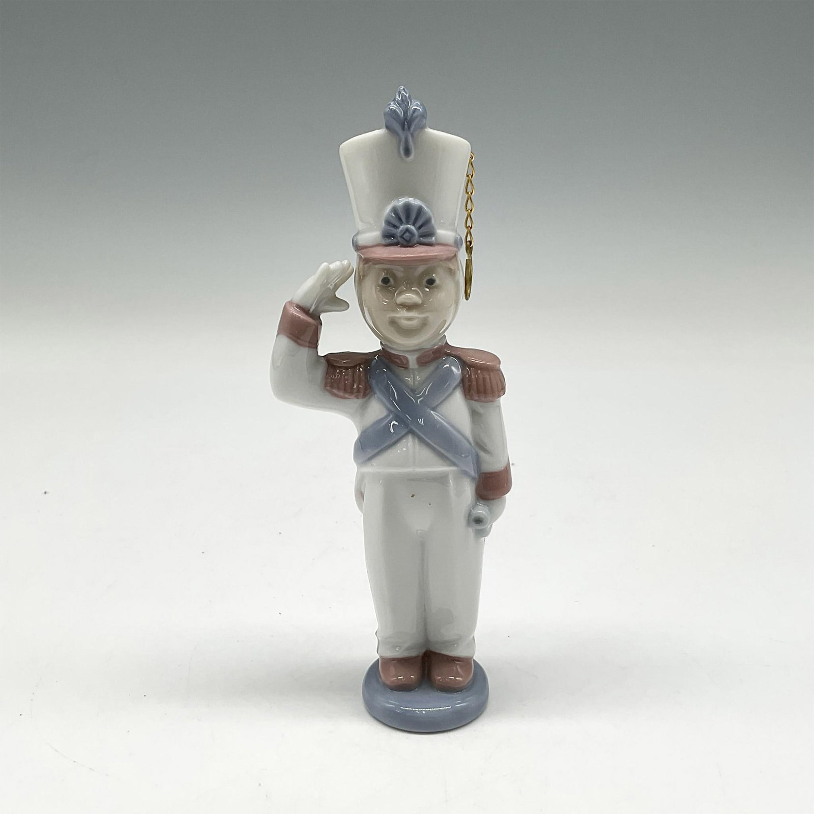Toy Soldier 1006345 - Lladro Porcelain Ornament: Glossy saluting figure colored in white, brown and blue. Lladro backstamp. This item has its original box: 6.5"L x 3.5"W x 4"H. Artist: Miguel Angel Santaeulalia Issued: 1996 - 1997 Dimensions: 2"L x 