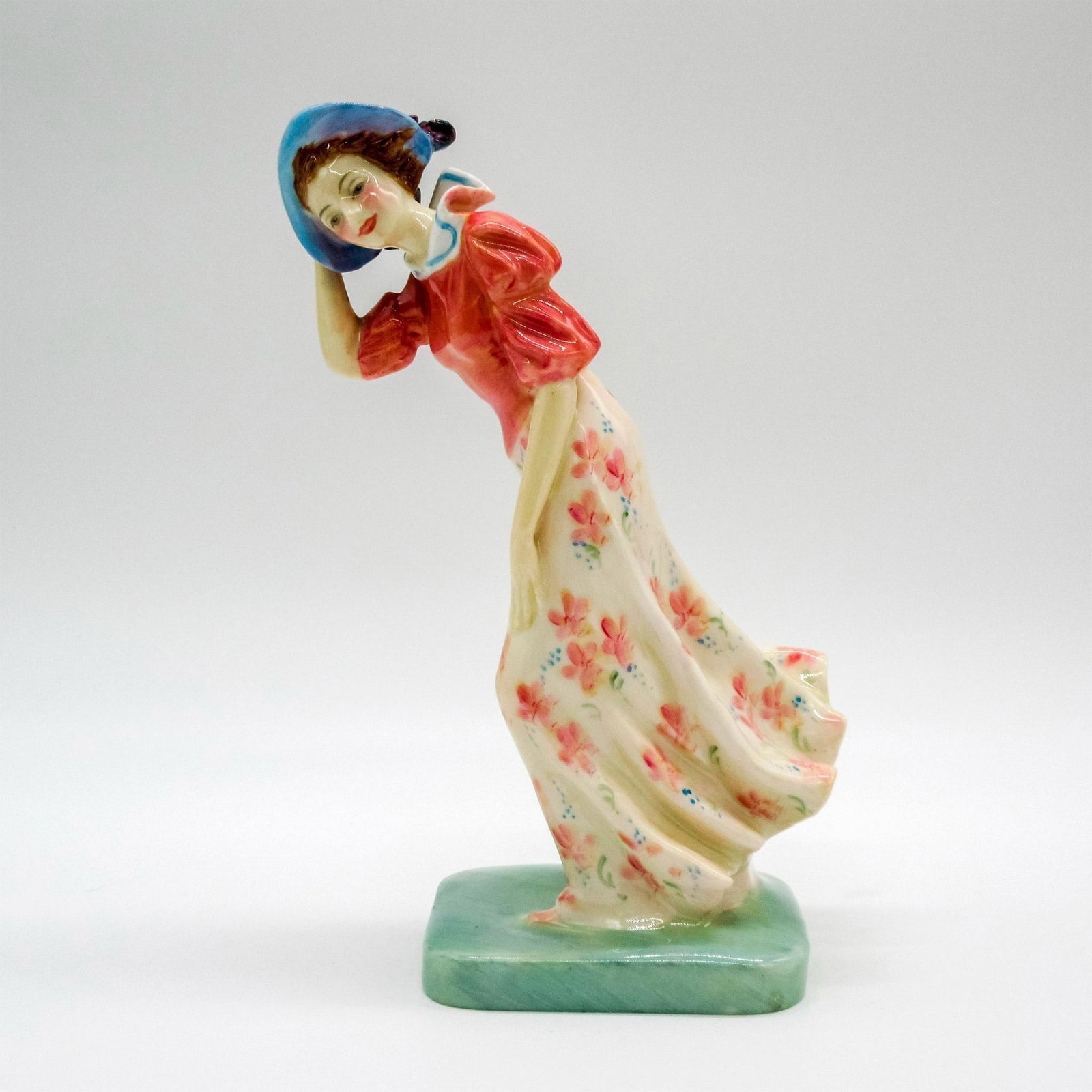Windflower HN1763 - Royal Doulton Figurine: First style variation; porcelain figure of a woman in the wind. Coral pink blouse with pink floral skirt. Royal Doulton backstamp. Artist: Leslie Harradine Issued: Circa 1936-1949 Dimensions: 2.5" L x