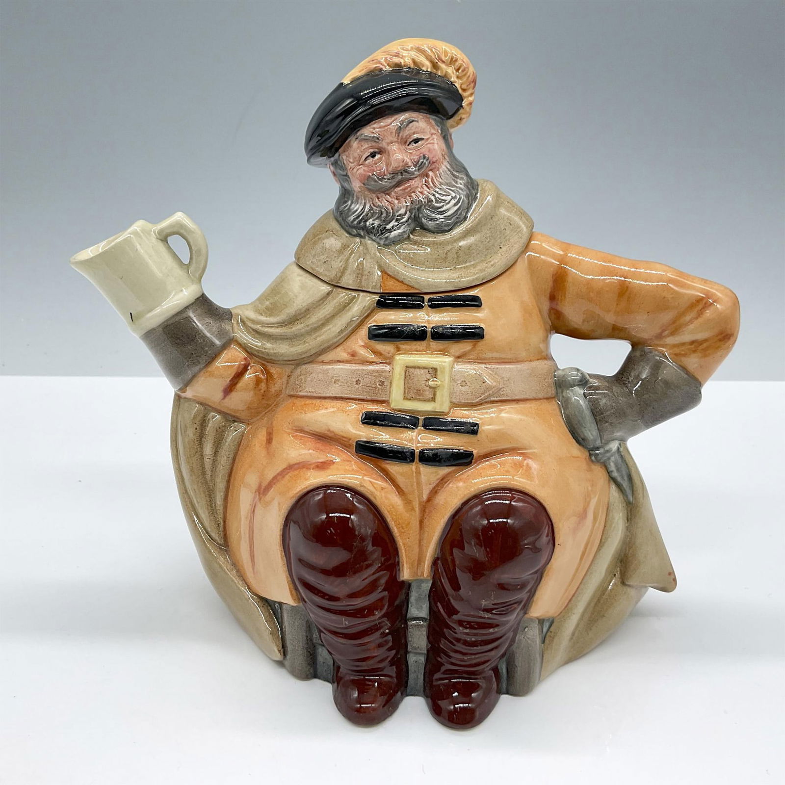 Royal Doulton Character Teapot, Falstaff D6854: Glazed finish. Features a fun teapot with the character in orange clothes and maroon boots holding a teacup. Royal Doulton backstamp. Artist: William K. Harper Issued: 1989-1991 Dimensions: 4.75''L x