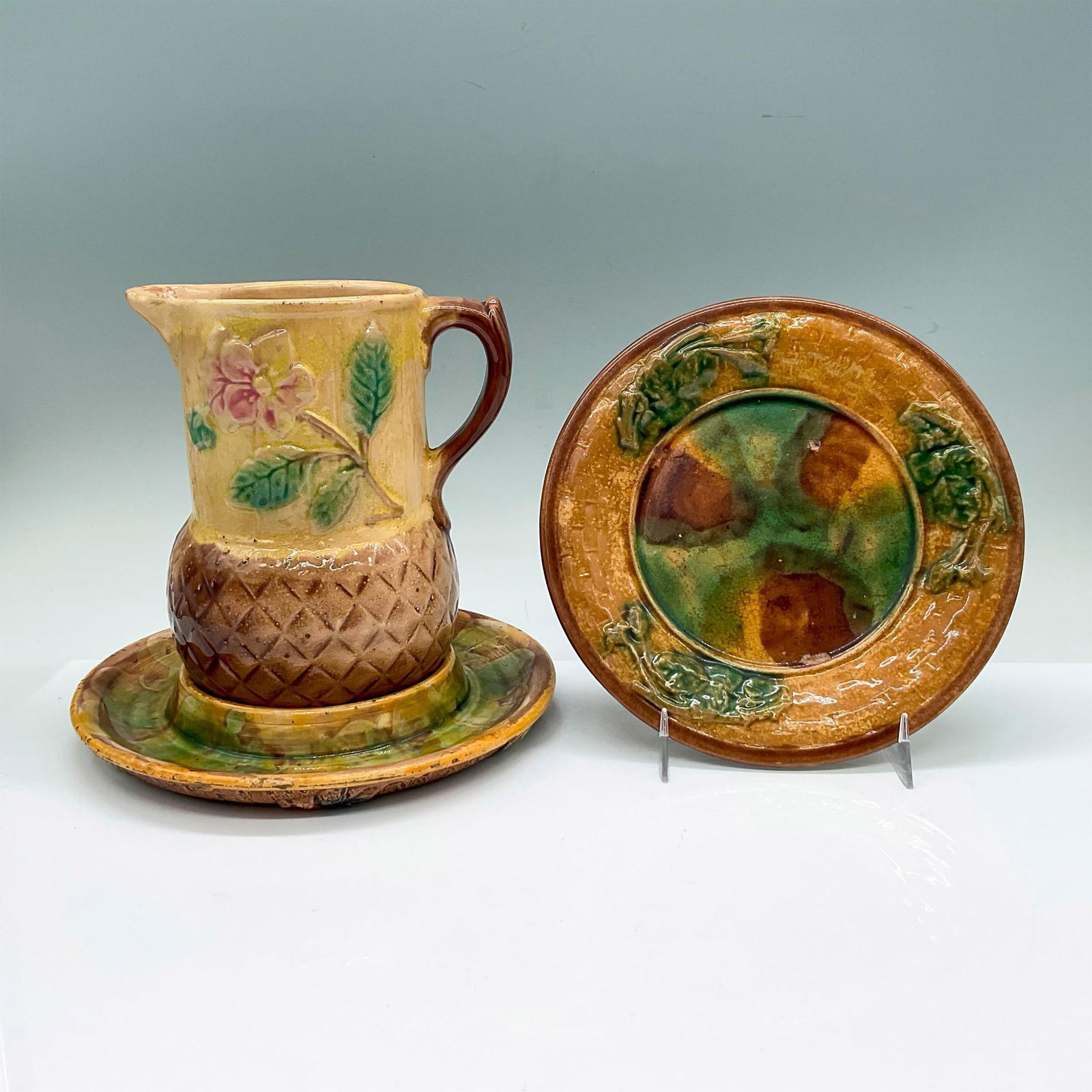 3pc Majolica Pottery Foliage Tableware: In a brown and yellow glaze in a leaf motif. A small GSH 6.75-inch round plate, a 7.25-inch round tray to hold a small pitcher. GSH plate: 0.5"H x 6.75" dia. Tray: 1"H x 7.25" dia. Pitcher: 5.25"L x 4