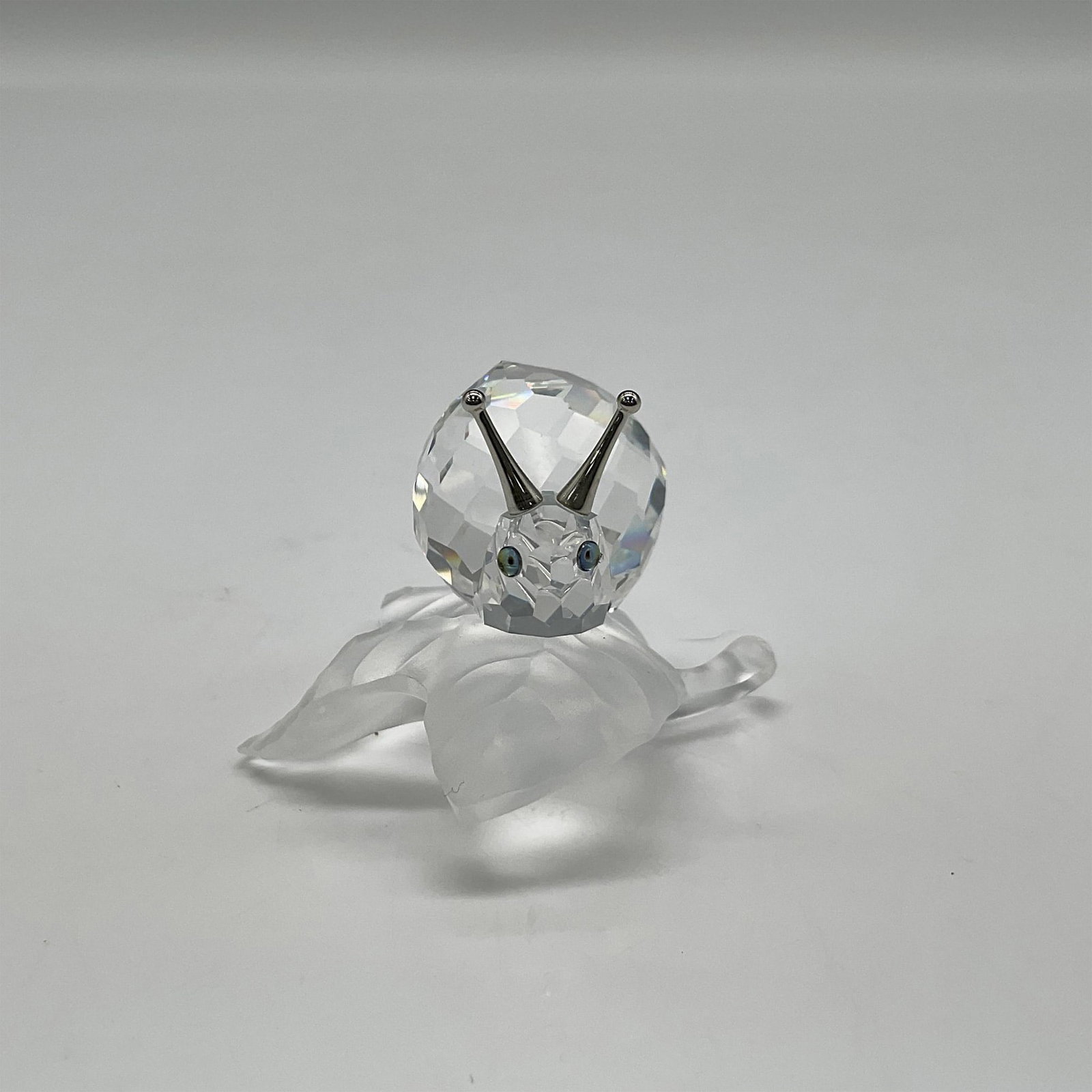 Swarovski Crystal Figurine, Snail on Vine Leaf: Depicts clear snail with crystal shell on top of opaque vine leaf. Rhodium antennas on top. Cantaloupe colored eyes with black pupils. Swarovski backstamp. 196501. This item has its original box: 4.5"