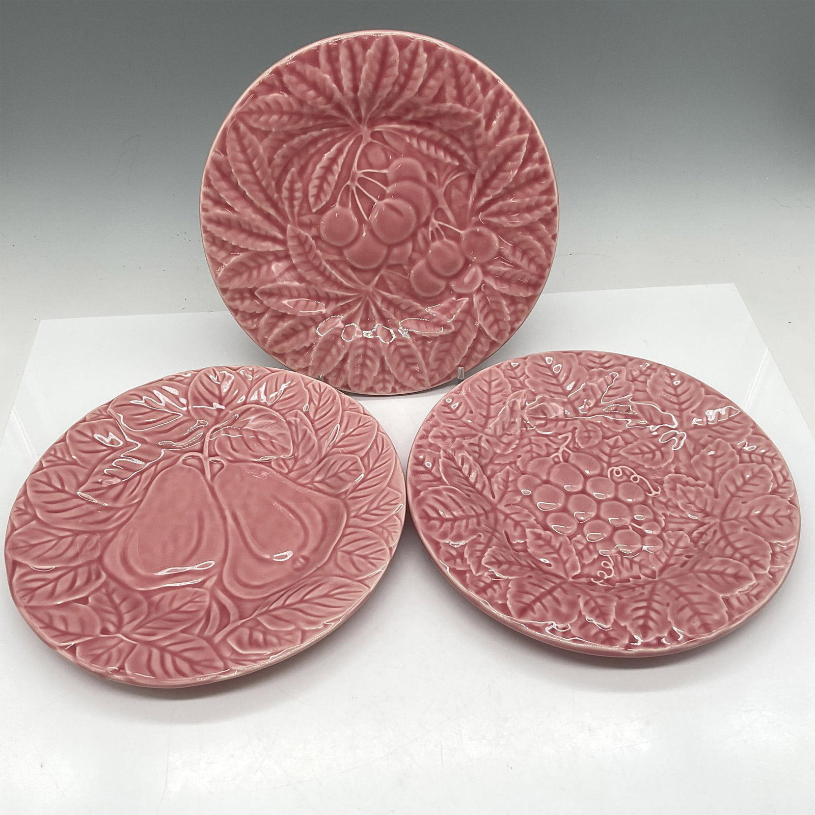 3pc Bordala Pinheiro Plates, Fruit: Raised design of grapes, pears and cherries on salmon pink coloration. Bordala Pinheiro Portugal backstamp. Issued: 20th century Dimensions: 1"H x 8" dia. Manufacturer: Bordala Country of Origin: Port