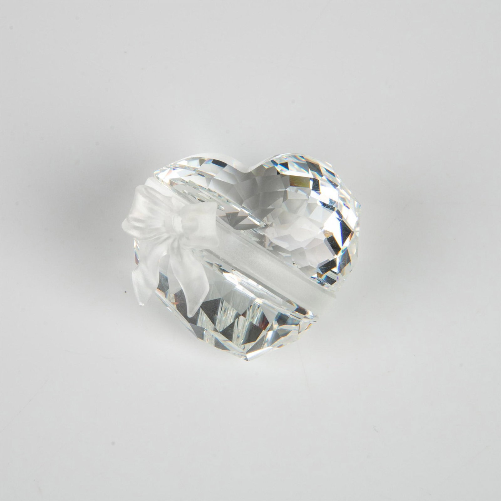 Swarovski Silver Crystal Figurine, Sweetheart 210035: A clear faceted figure of a round heart adorned with a matte ribbon. Part of the Exquisite Accents series. Swarovski marking. This item has its original box: 3.75"L x 3.75"W x 3"H. Artist: Edith Mair 