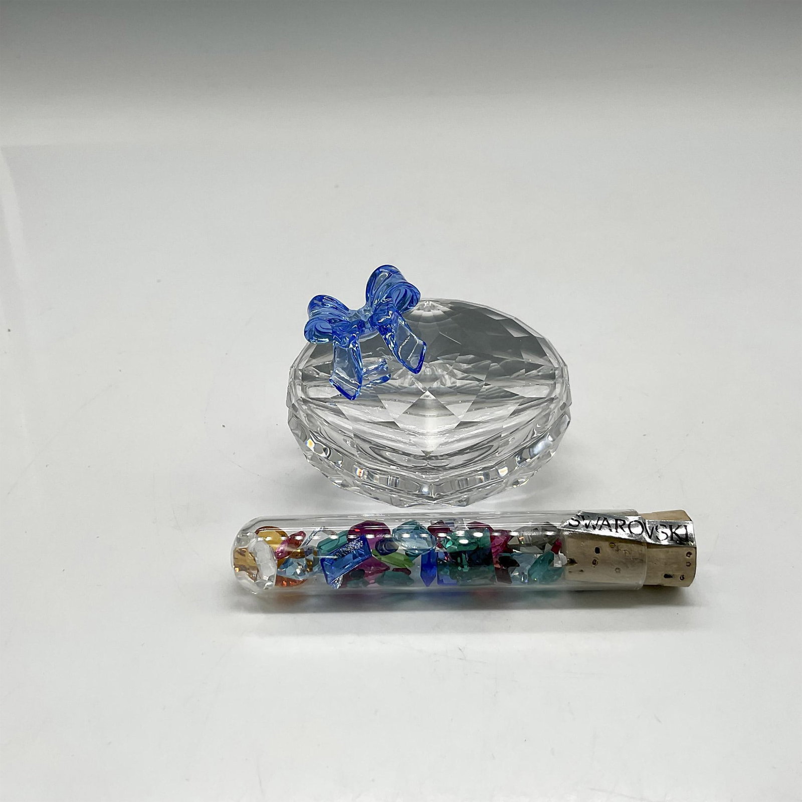 Swarovski Crystal Box, Jewel Sweetheart with Crystal Tube: Part of the Exquisite Accents group is a lidded heart shaped box adorned with blue crystal ribbon. Tube of multicolored crystals is included. Swarovski backstamp. 219966. This item has its original bo