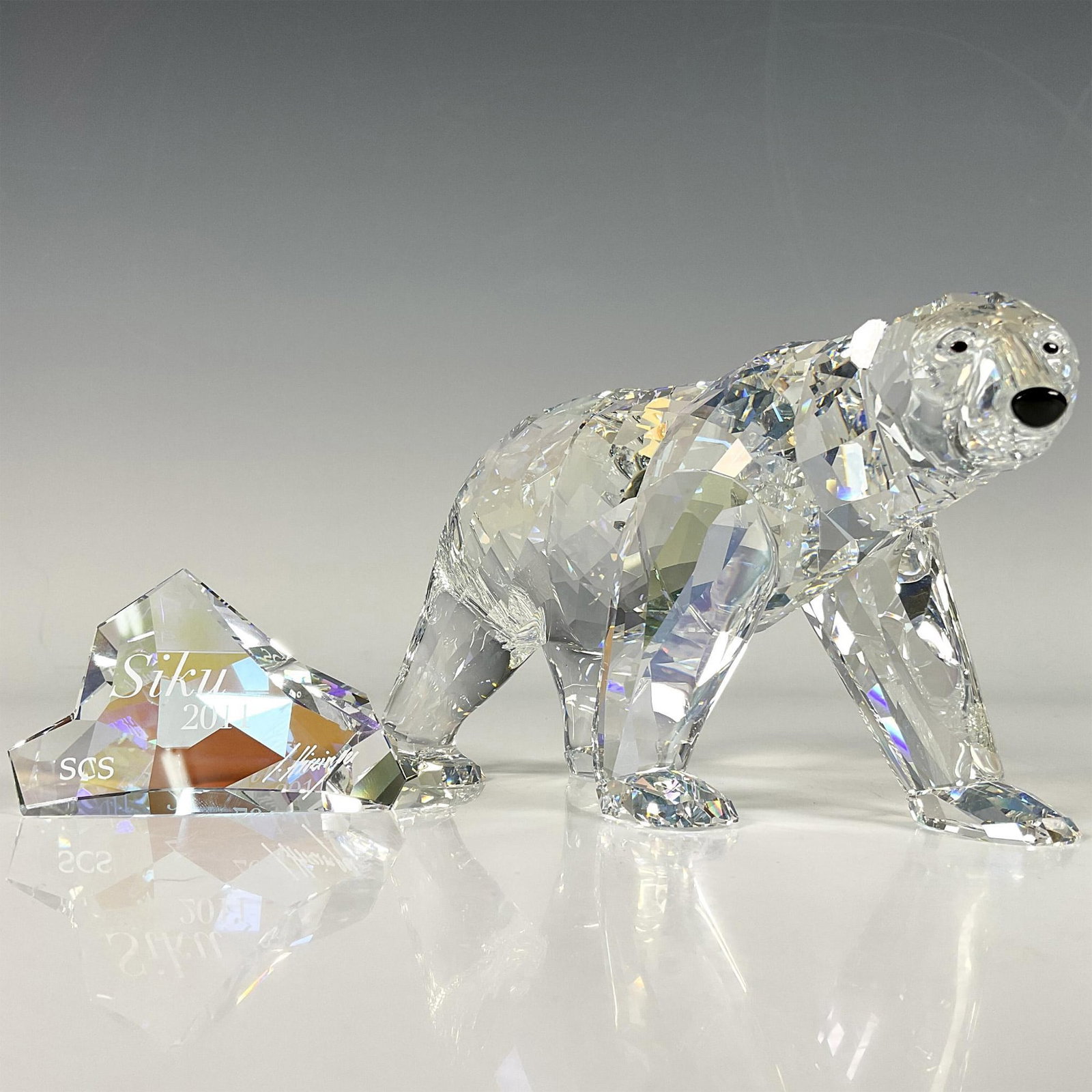 Swarovski Crystal Society Figurine + Plaque, Siku Polar Bear: A 2011 annual edition of an Artic bear in moonlight colored crystal with black crystal eyes and nose. Includes an iceberg formed plaque in aurora borealis crystal; Siku 2011, SCS, and artist name engr