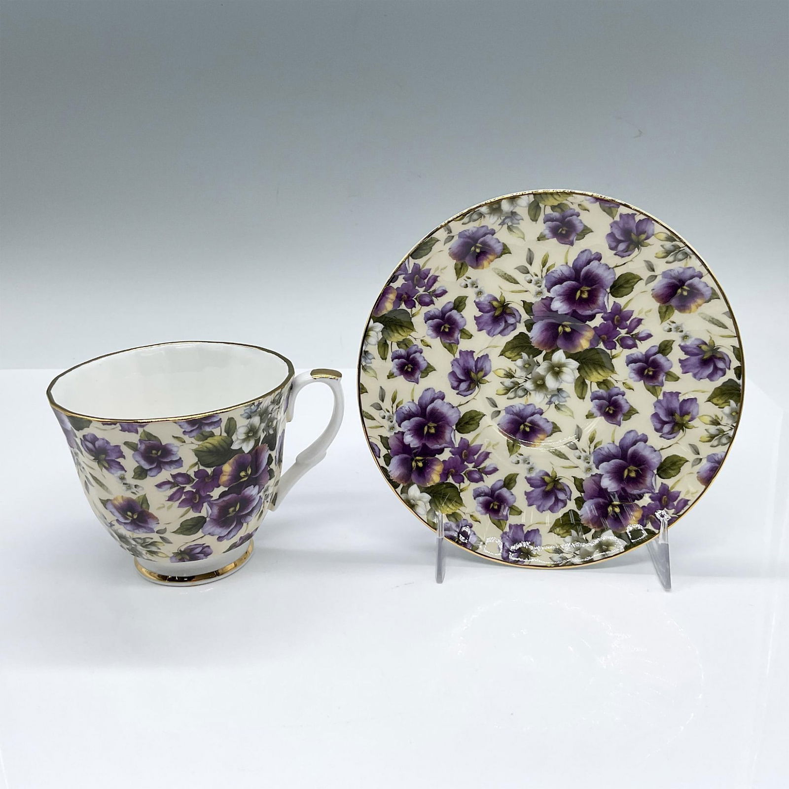 2pc Royale Garden Bone China Violet Tea Cup and Saucer: White and cream-colored English cup and saucer set for the Chintz Collection. Decorated with violets and gilded trim accents. Royale Garden backstamps. Cup: 4.25"L x 3.5"W x 3"H. Saucer: 0.75"H x 5.5"