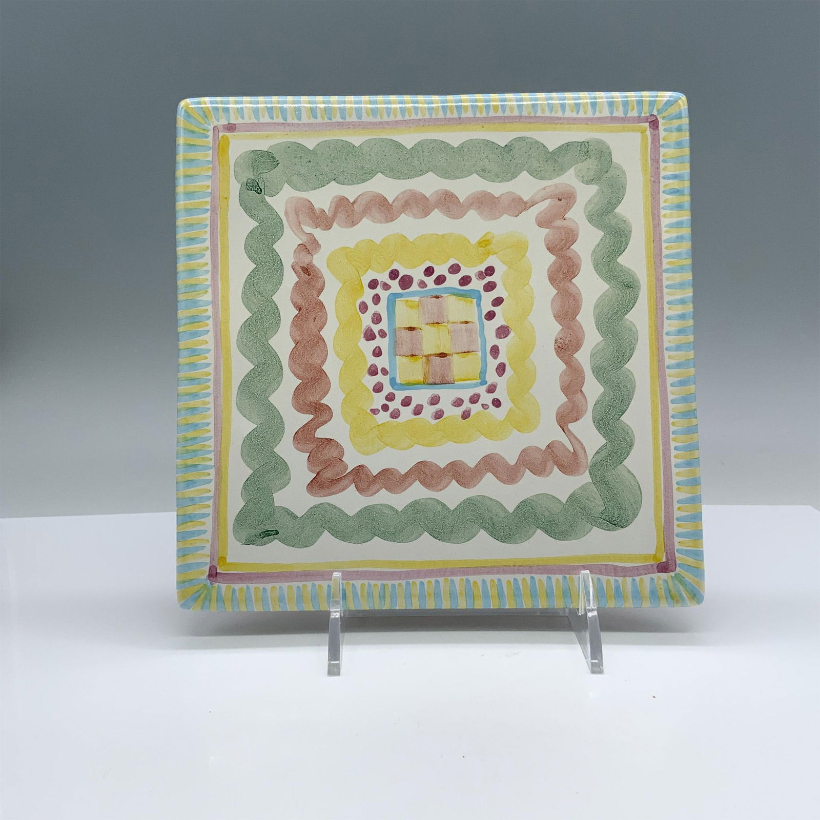 Victoria and Richard MacKenzie-Childs Ceramic Trivet Tile: Beautiful ceramic trivet tile decorated with pastel colors. The cork bottom is stamped with the Victoria and Richard MacKenzie-Childs backstamp. Issued: 20th c. Dimensions: 8"L x 8"W Manufacturer: Mac