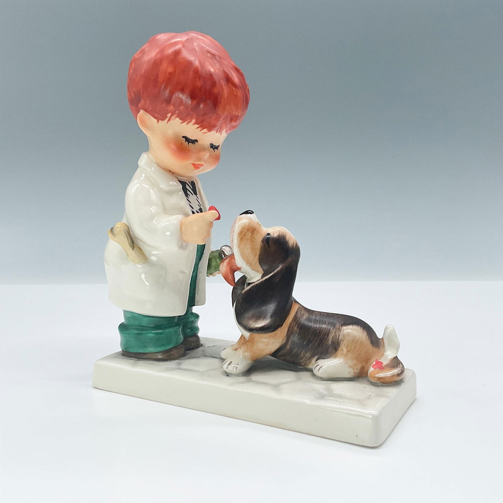 Goebel Hummel Figurine Veterinary Boy, Say Aaaah: Features a boy in a white coat giving his cute dog medicine. Hummel backstamp TMK 4. Issued: 1964-1972 Dimensions: 4.75"L x 2"W x 5.5"H Manufacturer: Goebel Hummel Country of Origin: Germany