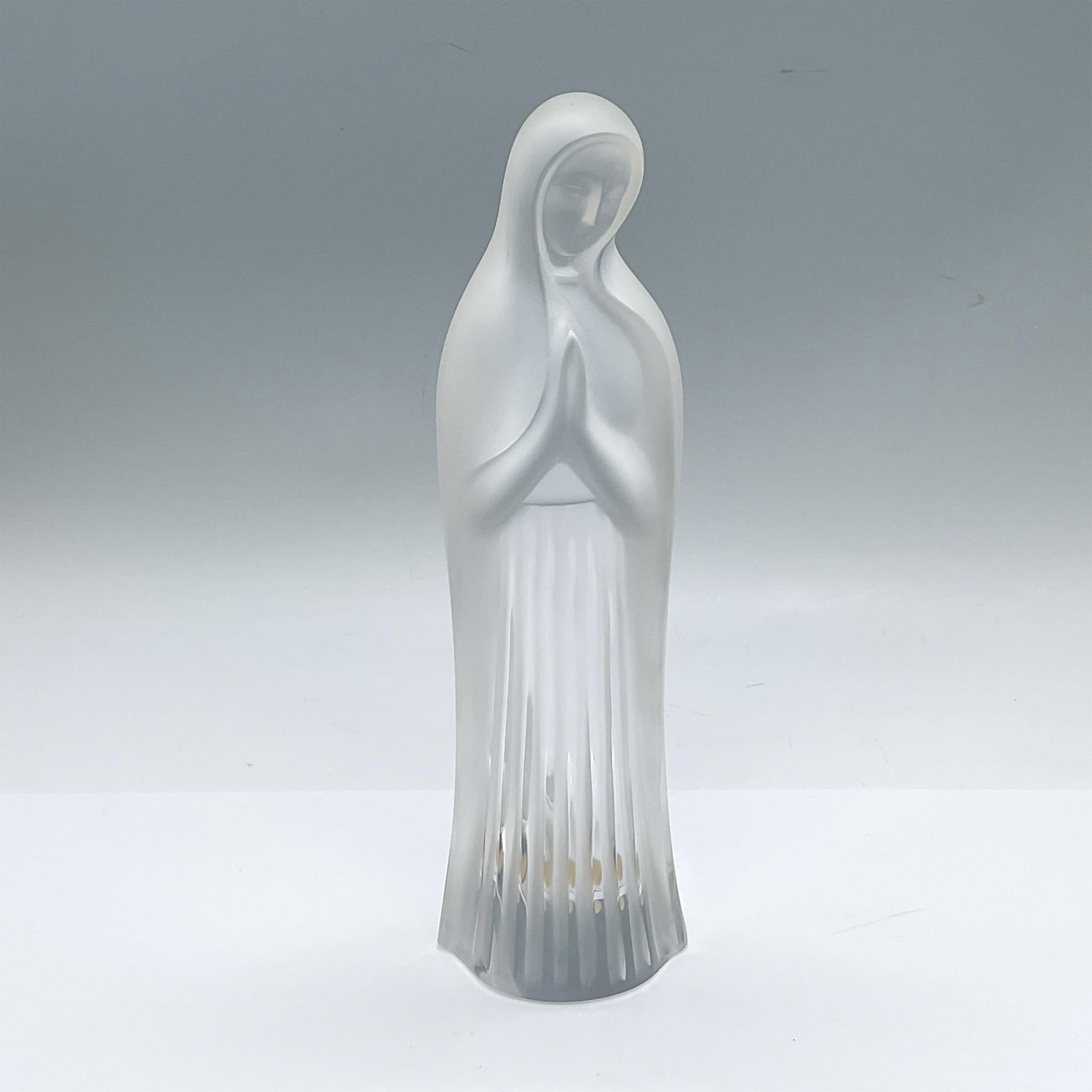 Lalique France Crystal Figurine, Madonna: Clear and satin figure of the Virgin Mary, depicted with her hands together. Lalique France marked. Issued: 20th century Dimensions: 3.25"L x 3"W x 9.75"H Manufacturer: Lalique Country of Origin: Fran