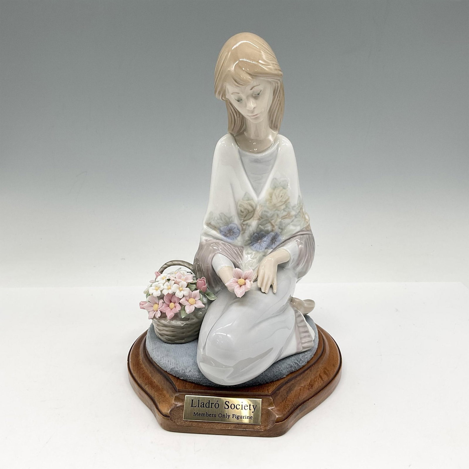 Flower Song 1007607 + Base - Lladro Porcelain Figurine: Glossy figure. Young woman seated next to a basket of flowers. Collectors Society Piece from 1988. Lladro backstamp. This item has a base included: 5.5"L x 6"W x 1"H. Artist: Juan Huert Issued: 1988-1