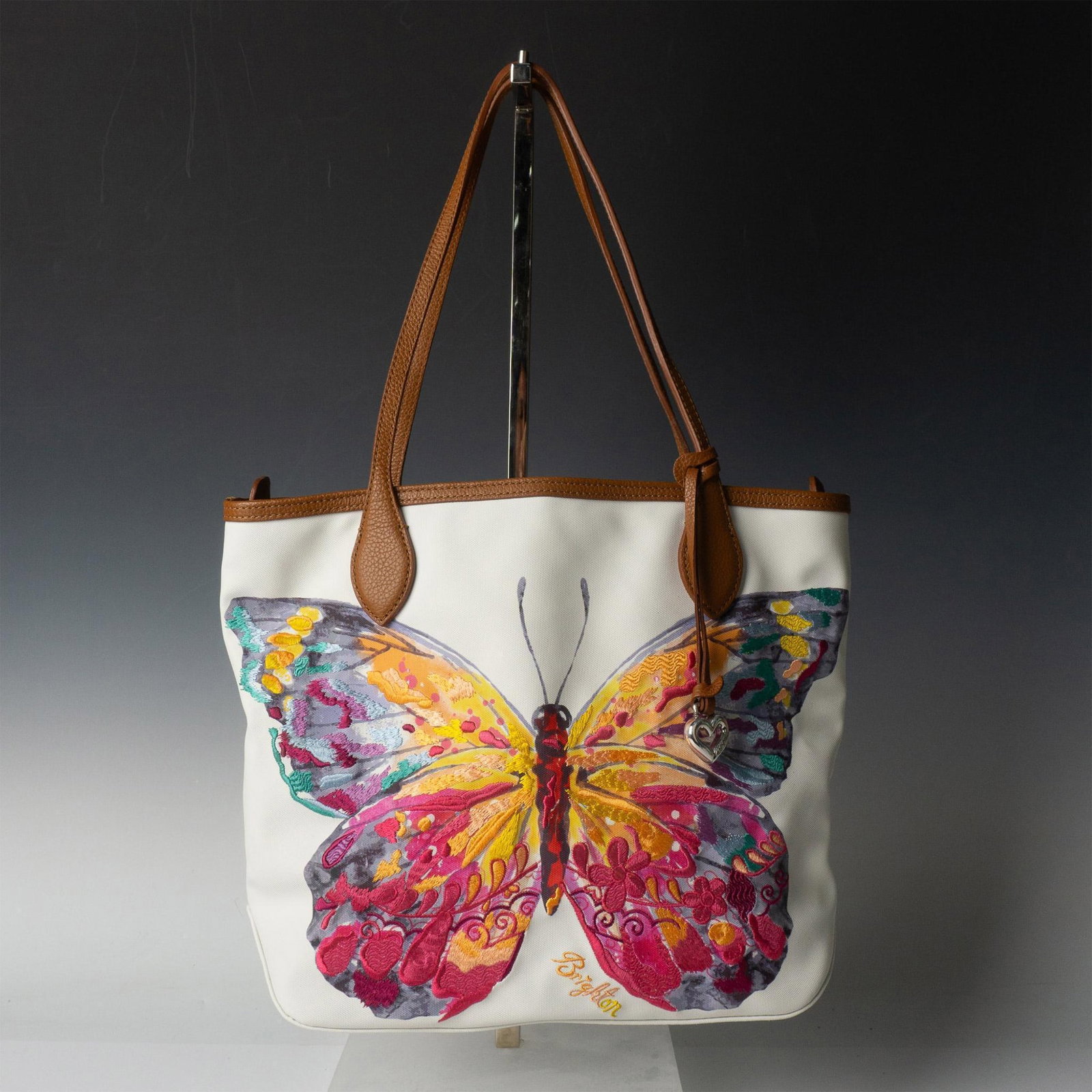 Brighton Canvas Tote Handbag, Colorful Butterfly: White coated canvas with brown leather trim and shoulder straps decorated with large colorful butterfly. Interior pockets, zippered top closure. Length of shoulder straps is 10"L. Brighton leather pat