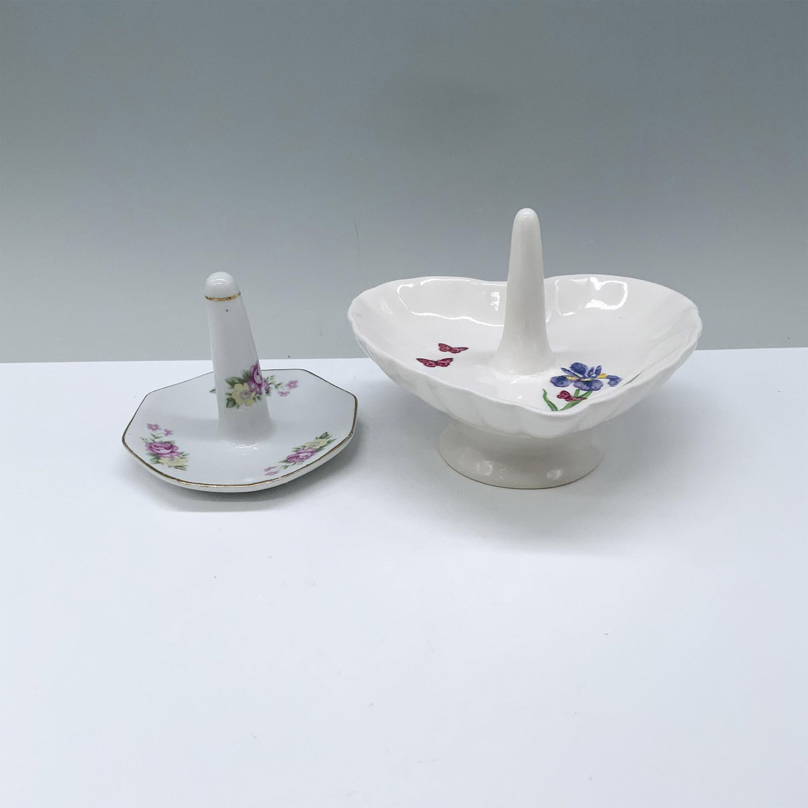 2pc Ceramic White Ring Holders: One heart-shaped with butterfly and floral motifs, the other octagonal with pink roses and yellow hibiscus. Dimensions of the largest item: 5"L x 4.75"W x 3.75"H.